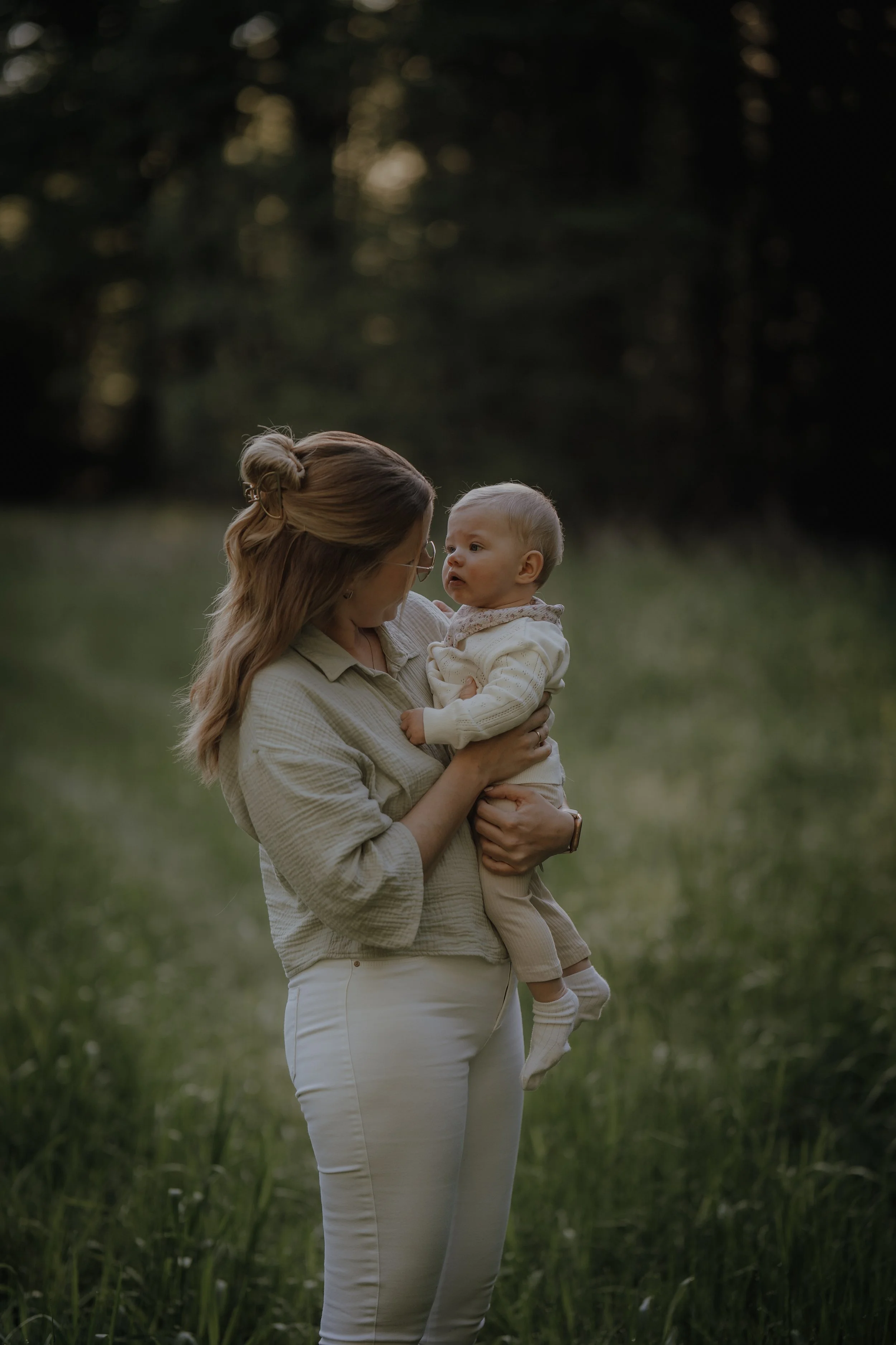 Eine Frau hält ein kleines Kind im Grünen bei Sonnenuntergang im Freien, umgeben von Bäumen und Gras.