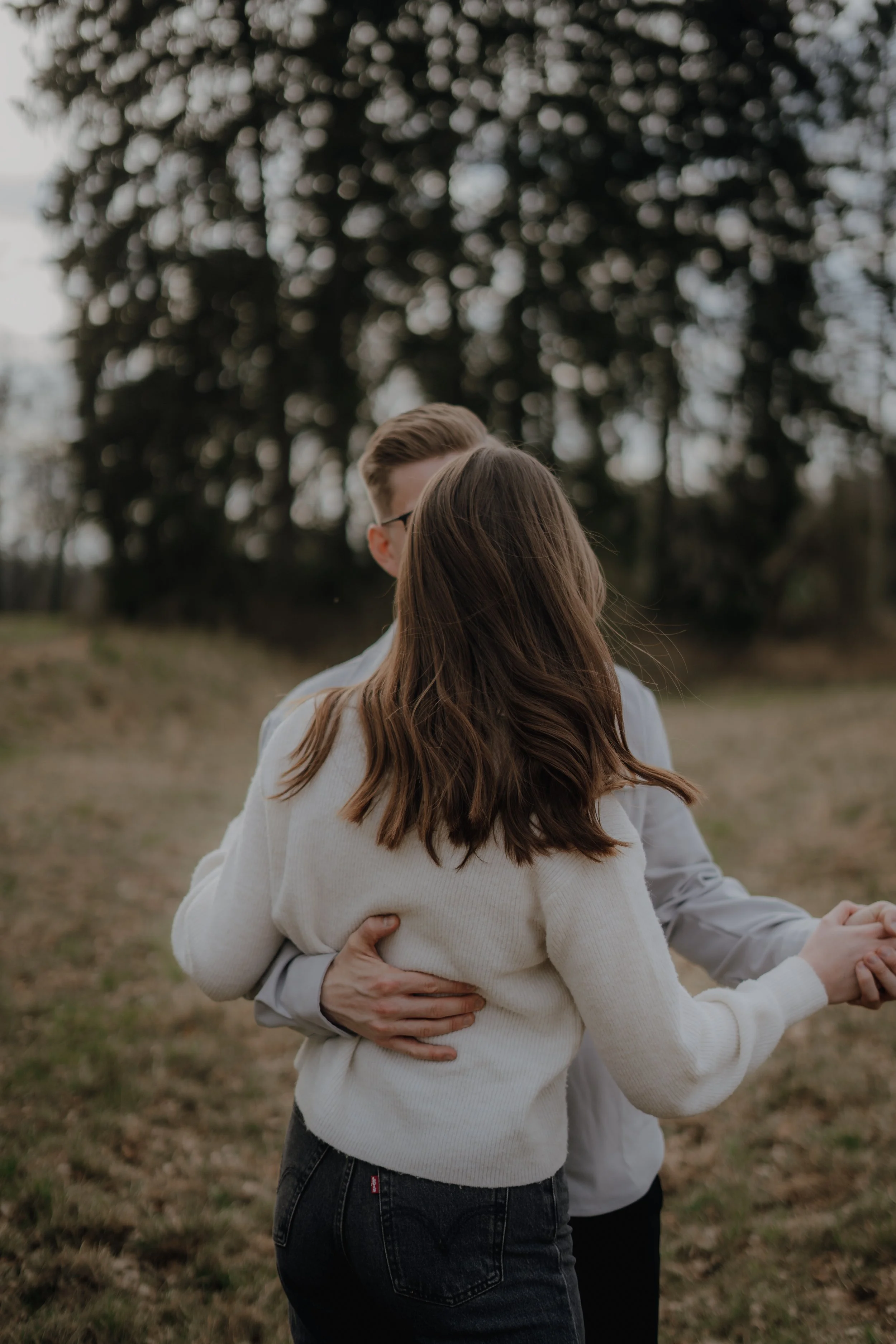 Ein Paar tanzt im Freien auf einer Wiese, umgeben von Bäumen, bei Sonnenuntergang.