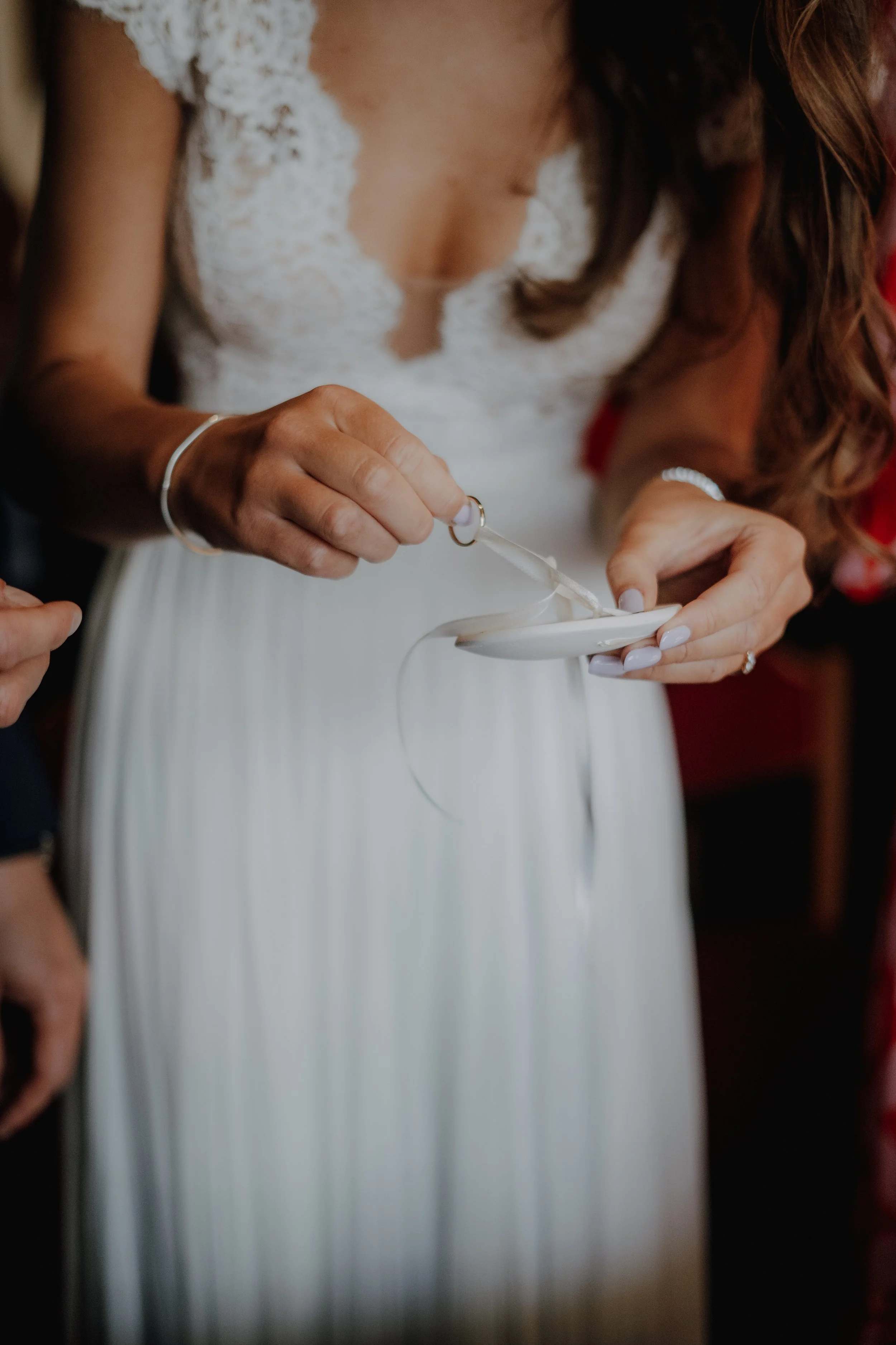 Frau in weißem Brautkleid beim Einstecken eines Eherings in ein Amulett