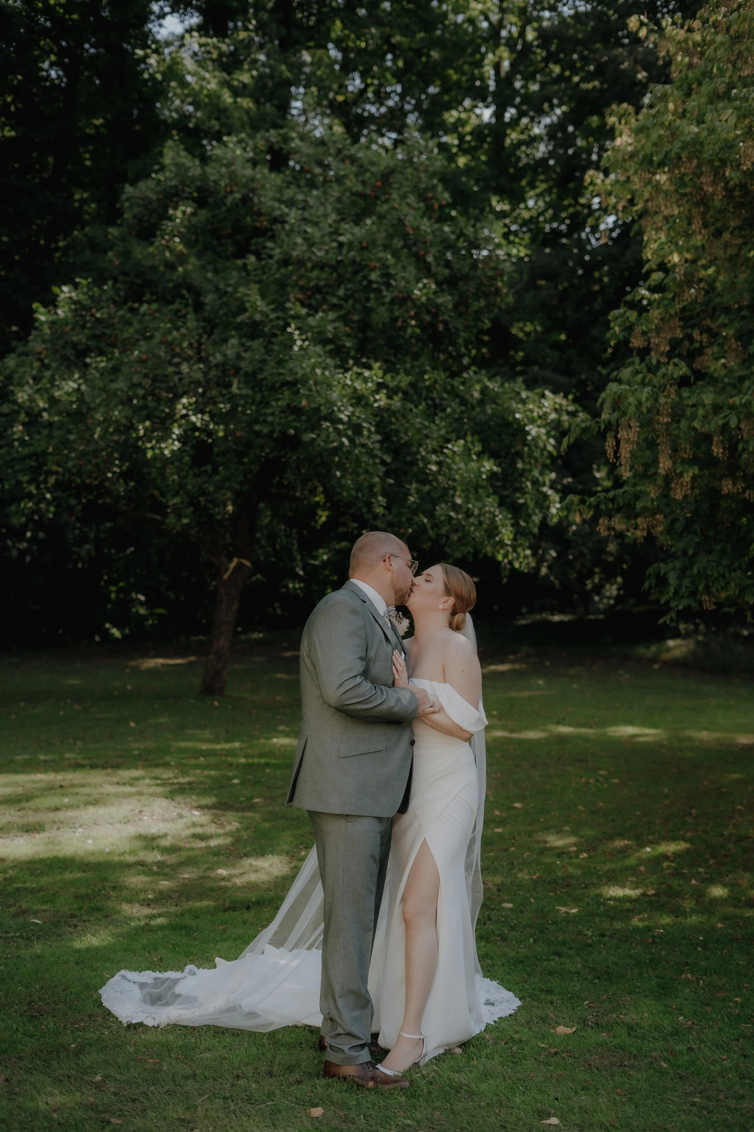 Ein Paar, das sich bei einer Hochzeit küsst, steht im Grünen unter Bäumen.