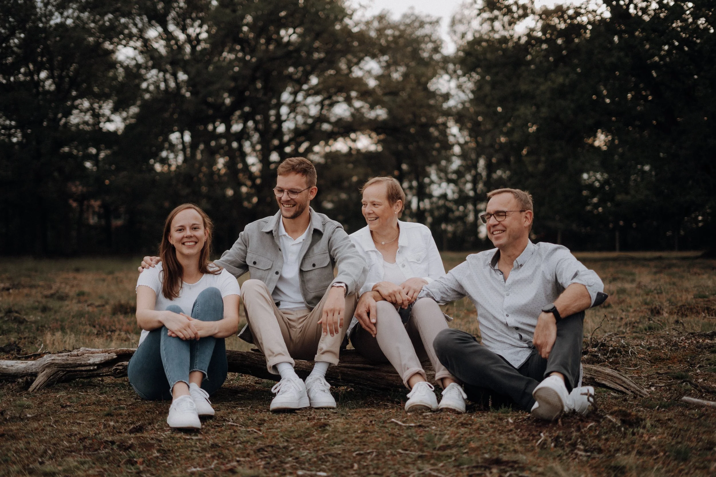 Vier Menschen sitzen im Freien auf dem Boden und lachen zusammen, im Hintergrund Bäume, es ist vermutlich Abend.