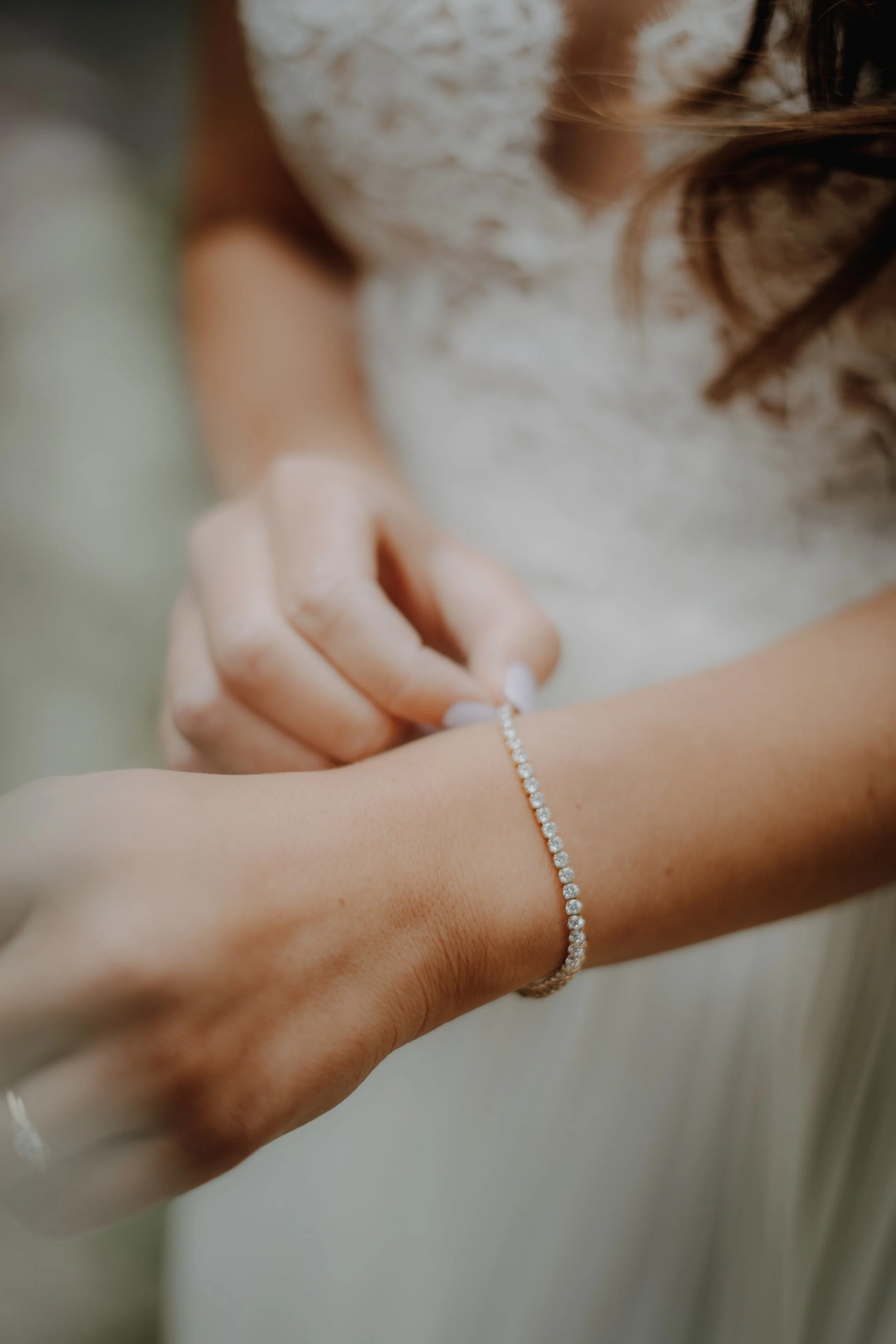 Nahaufnahme eines Handgelenks mit einem Diamantring und einem Diamantarmband, eine Person legt den Ring an.