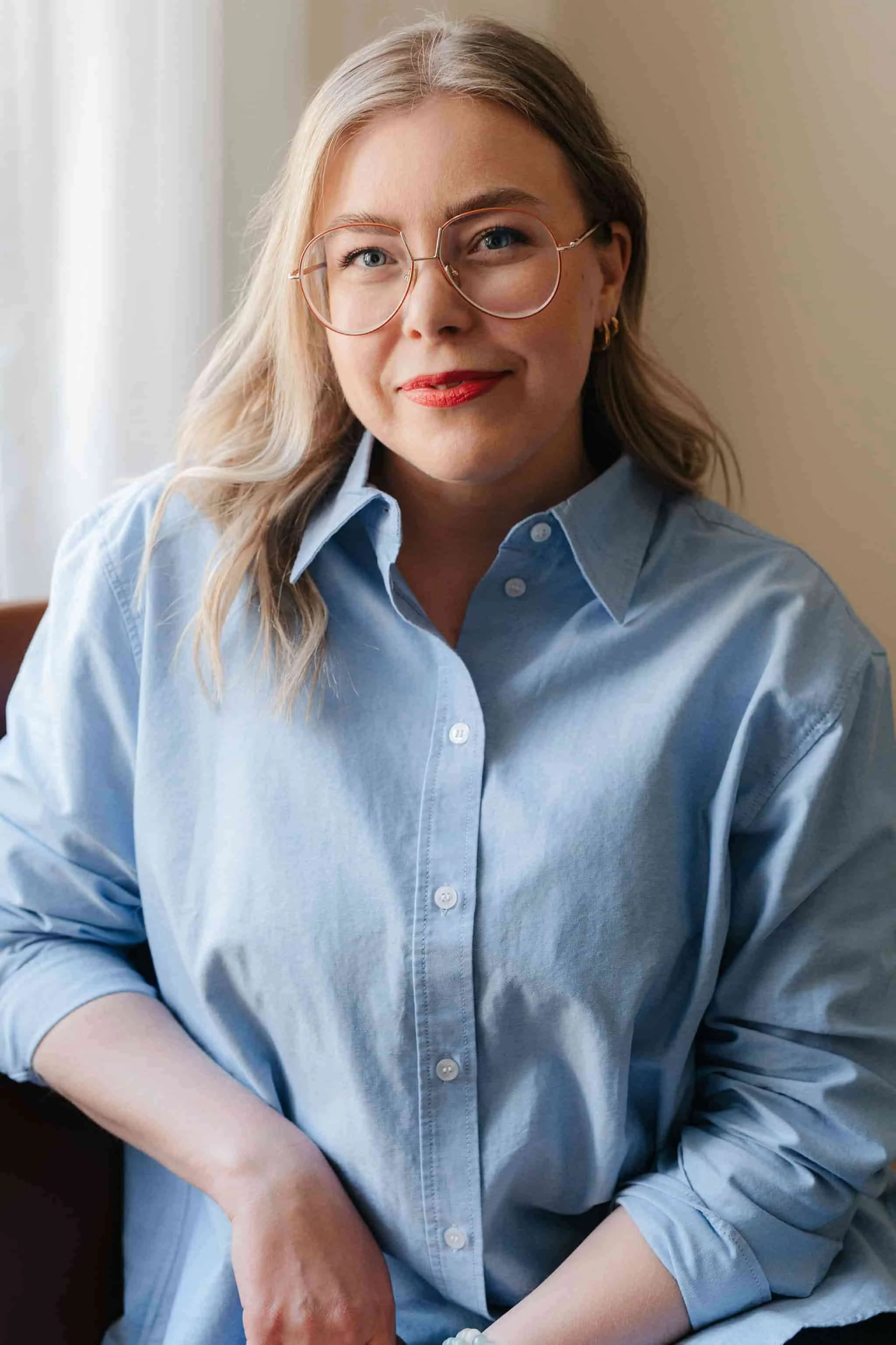 Nuorehko nainen puserossa ja silmälaseissa istuu sisätiloissa.