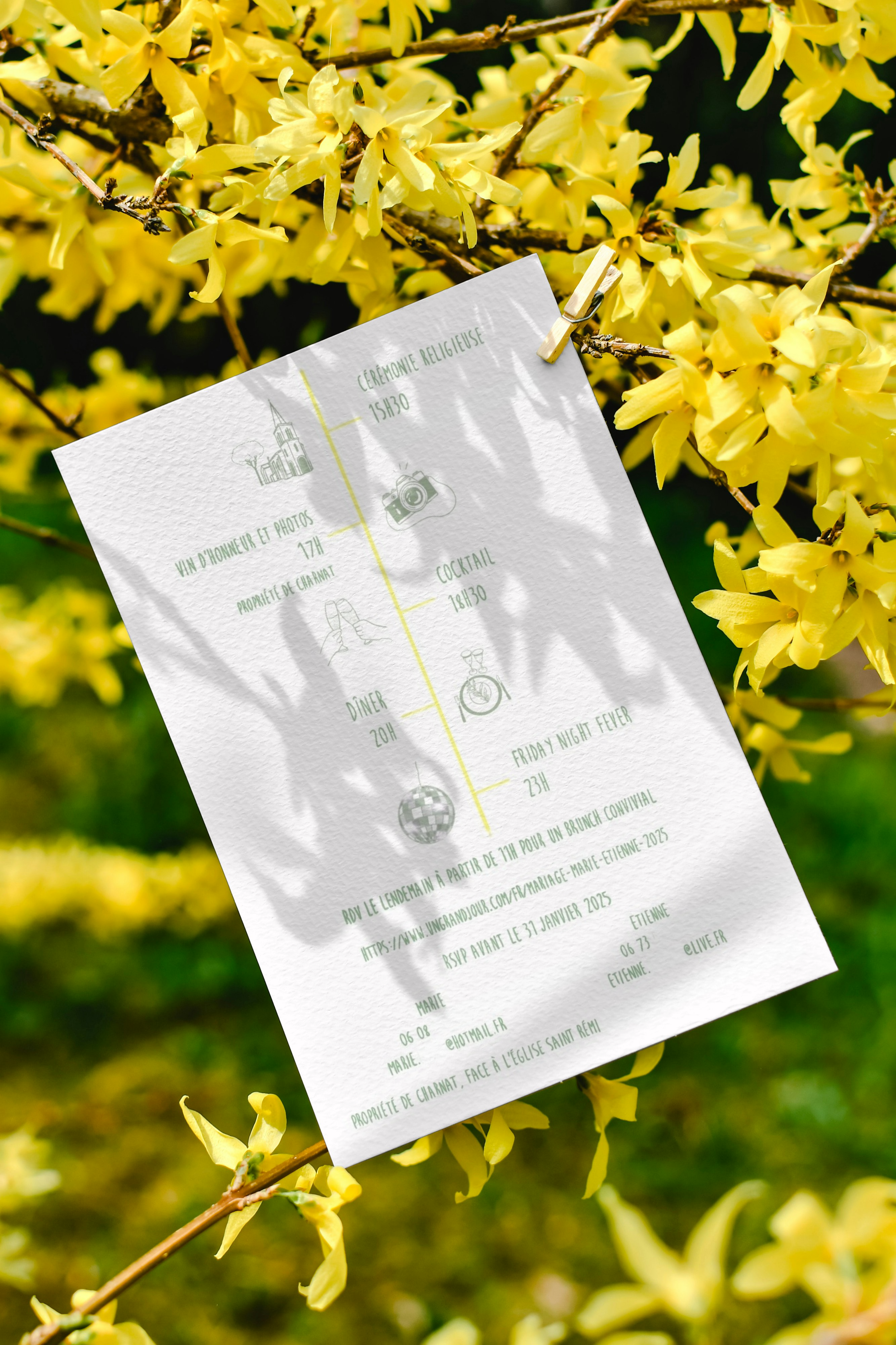 Une invitation à un mariage affiche, suspendue à une branche de forsythia en fleurs jaunes, dans un jardin ensoleillé.