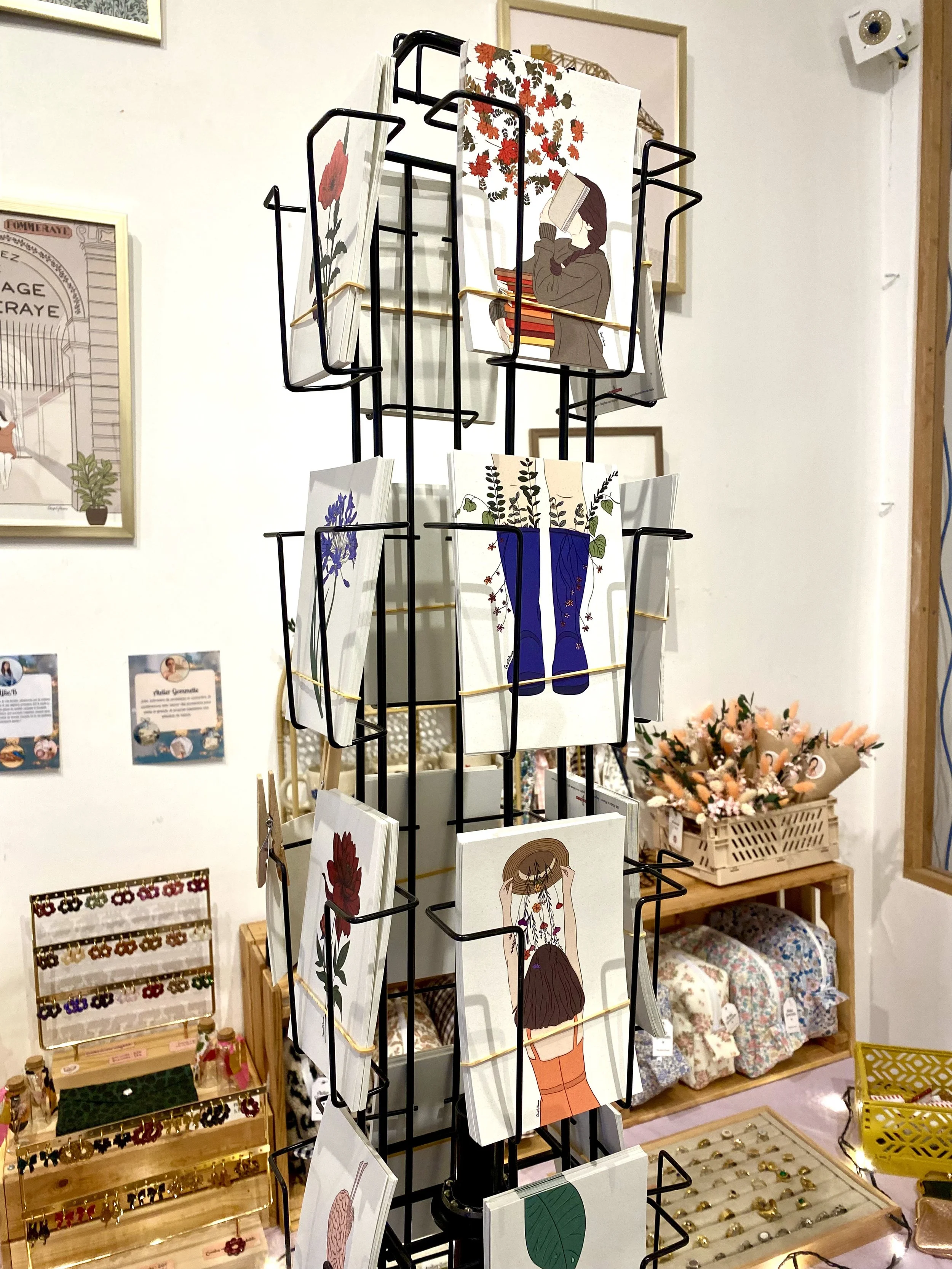 Étagère tournante avec des cartes illustrées de femmes et de fleurs dans une boutique de décoration ou de cadeaux.