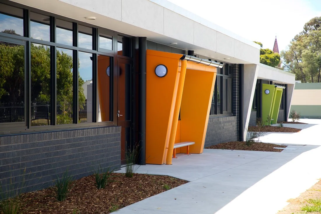 Modern building exterior with colorful, angled bus shelters in orange and green along sidewalk.