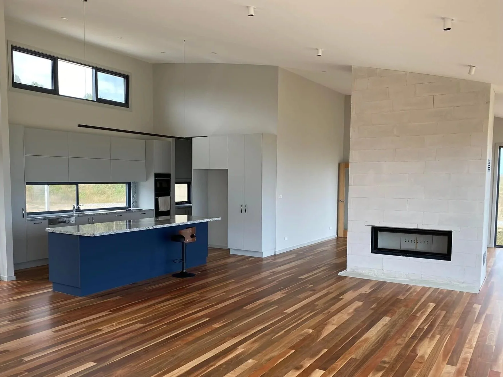 Open-concept living room and kitchen with wooden floors, white cabinetry, a blue kitchen island, and a stone fireplace.