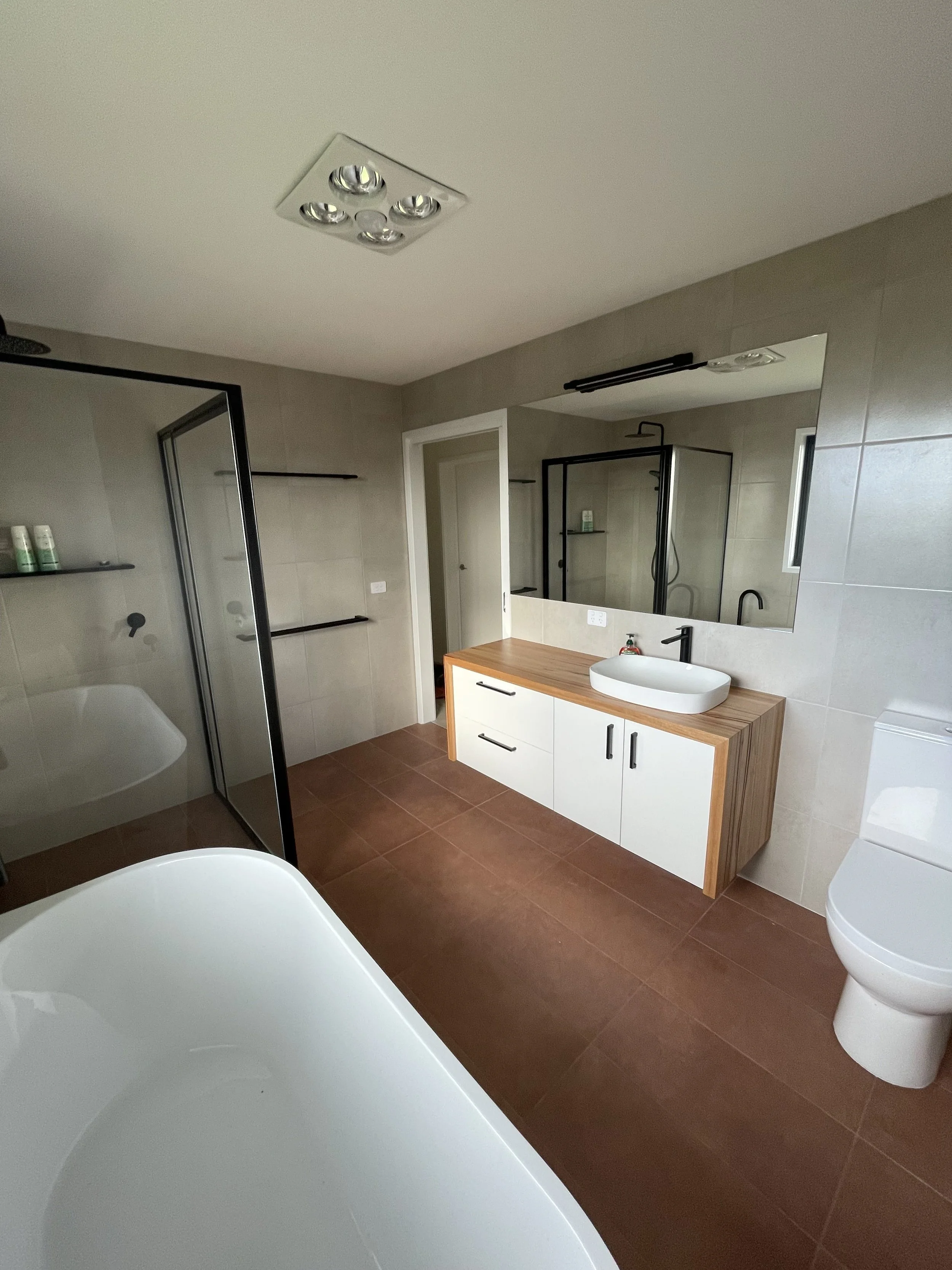 Modern bathroom with a bathtub, a vanity with a sink, a large mirror, a toilet, and a glass shower enclosure, with beige tiled walls and brown tiled floor.