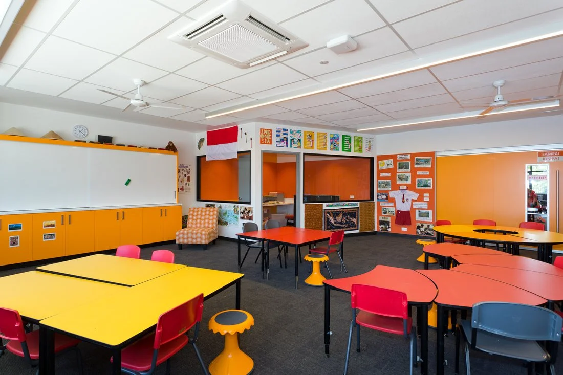 A colorful classroom with orange, red, and yellow furniture, display boards, and a whiteboard.