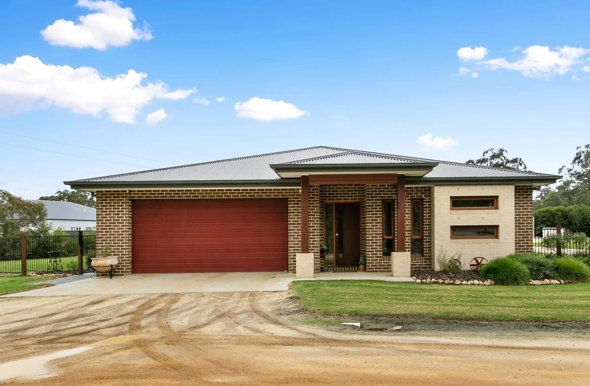 Modern single-story brick house with a red garage door and two narrow windows beside the front door, surrounded by a lawn and garden bed, under a partly cloudy sky.