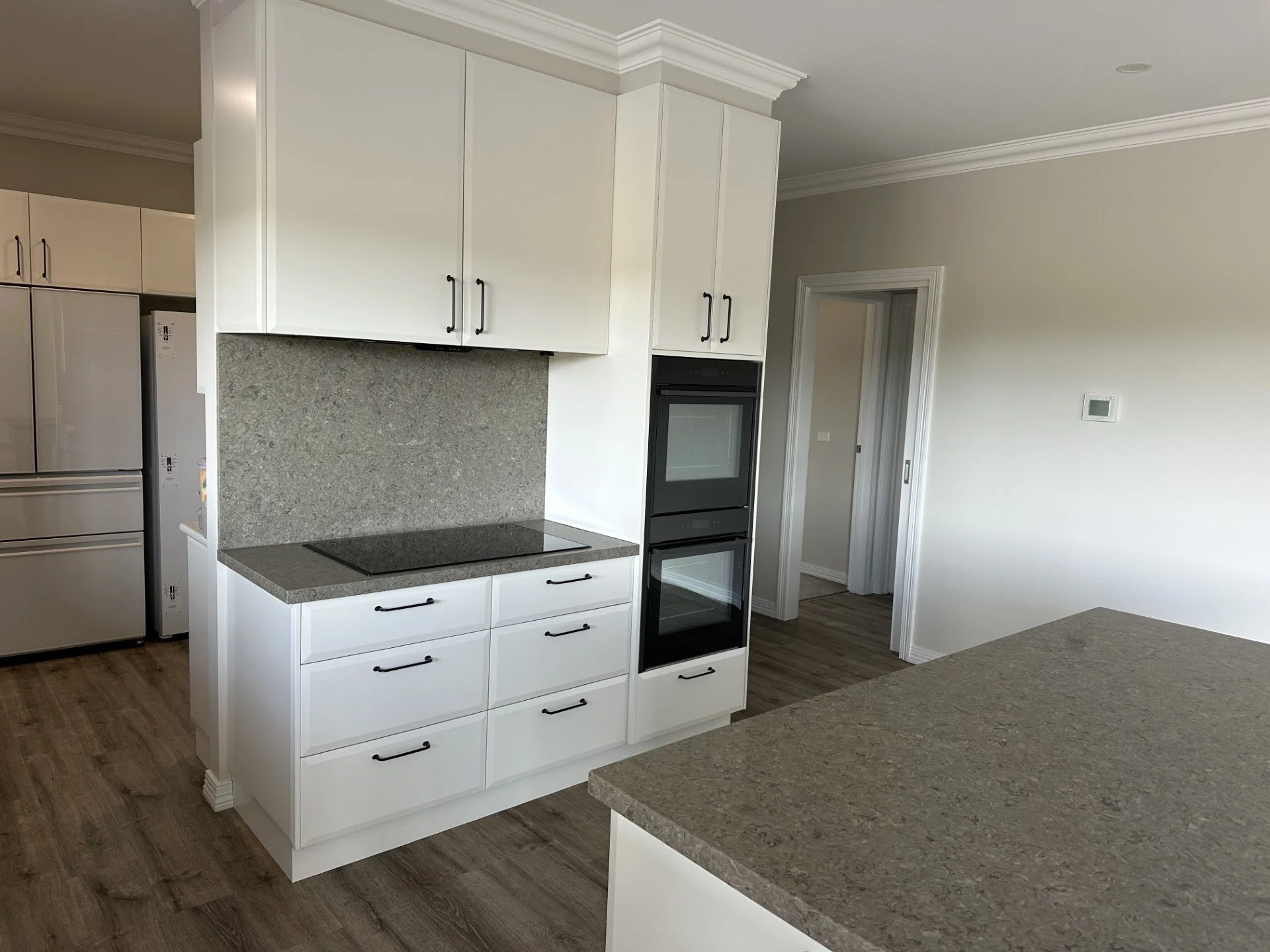 Modern kitchen with white cabinets, granite countertops, a black stovetop, and built-in oven, with hardwood floors and a doorway leading to a hallway.