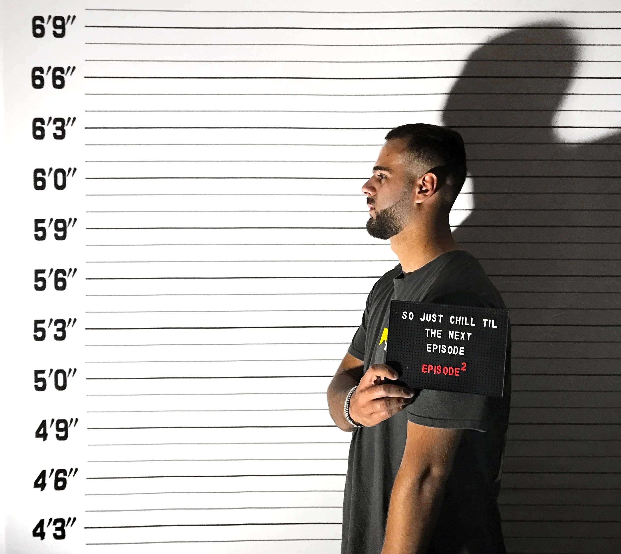 Homme debout à côté d'un mur avec une ligne de hauteur de portrait, tenant un panneau avec un message écrit en anglais.