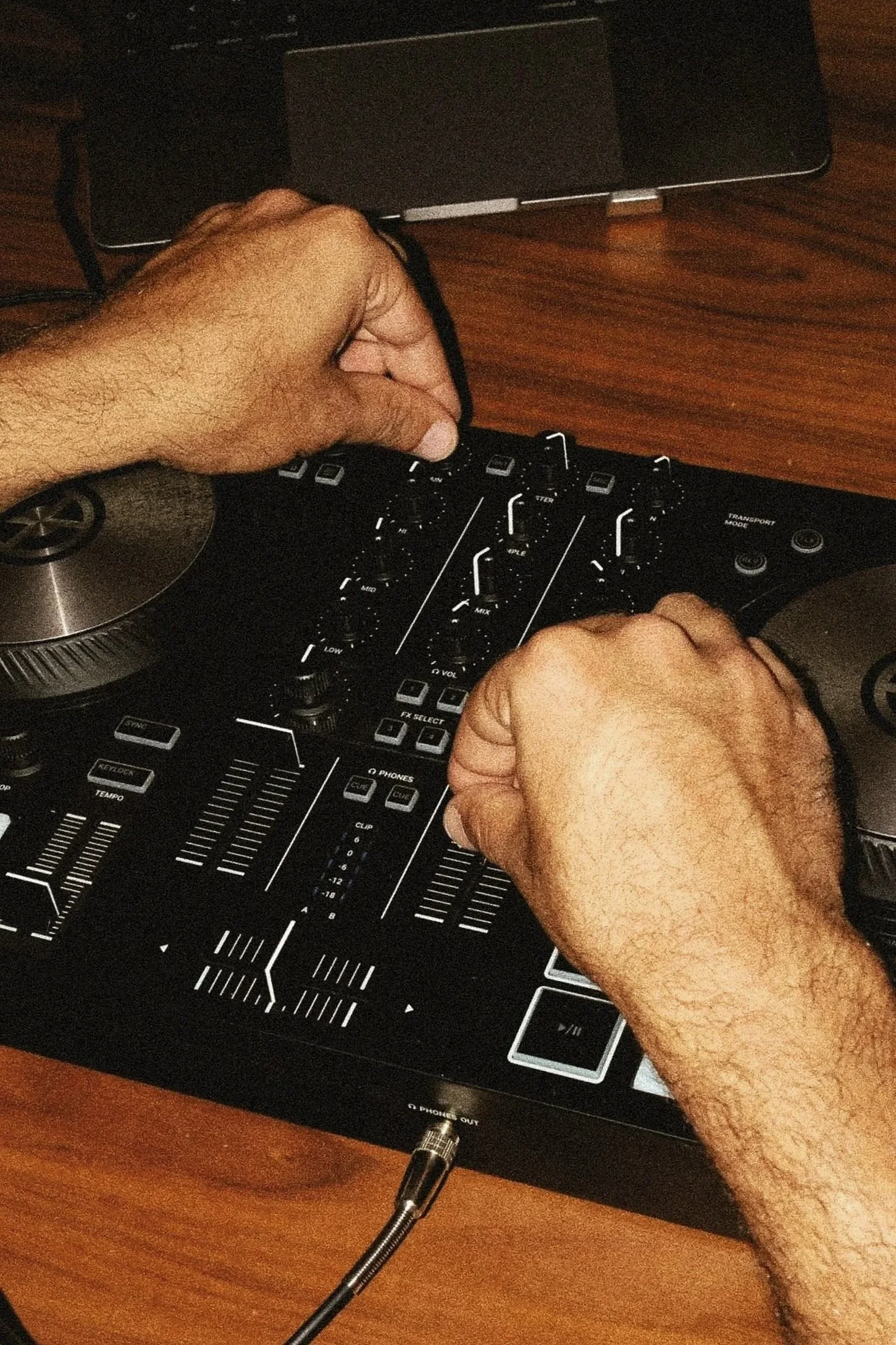 Main manipulant un contrôleur de DJ ou une console de mixage sur une surface en bois.