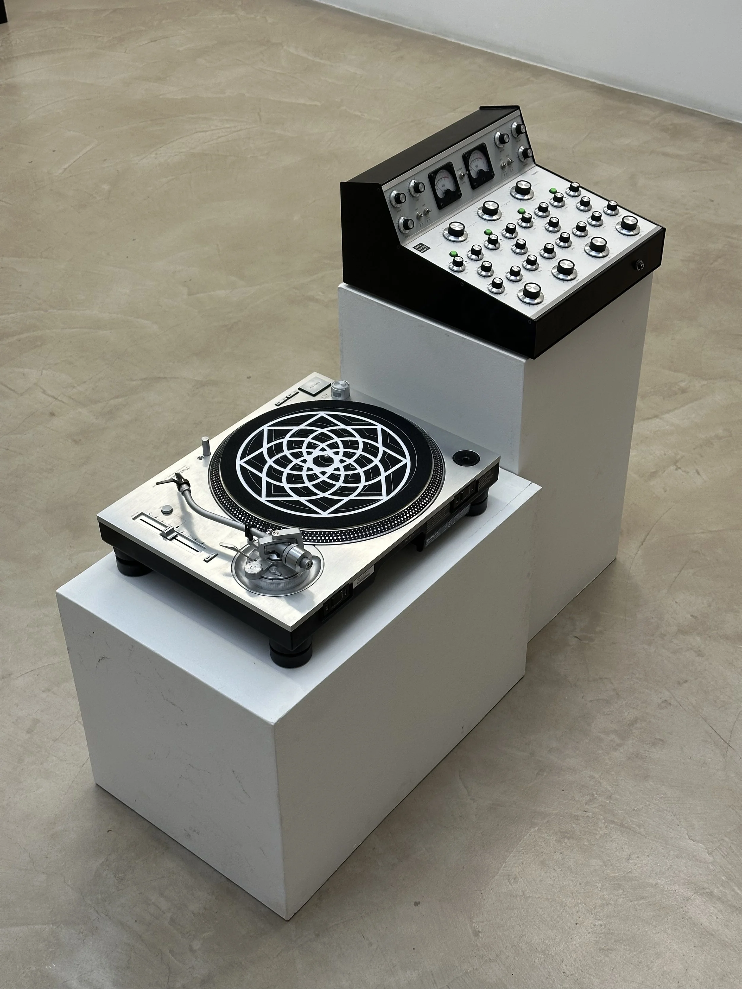 Un tourne-disque avec une platine et une console de mixage sur un socle blanc, dans une pièce avec un sol en béton.