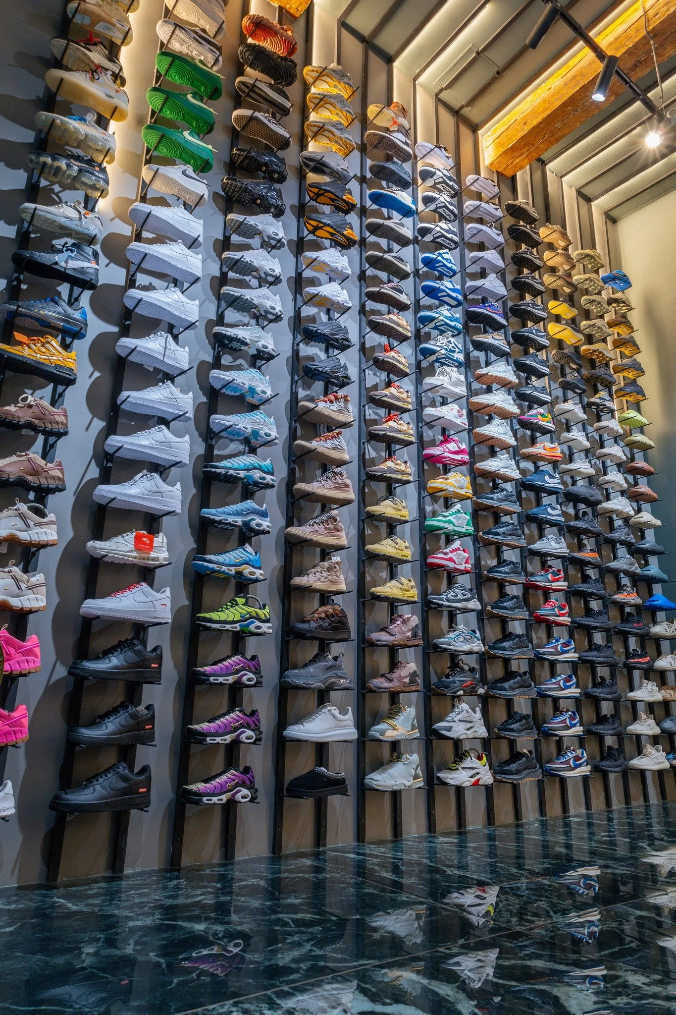 Une grande murale avec de nombreuses paires de baskets de différentes couleurs et styles, organisées verticalement sur des supports dans un magasin de chaussures.