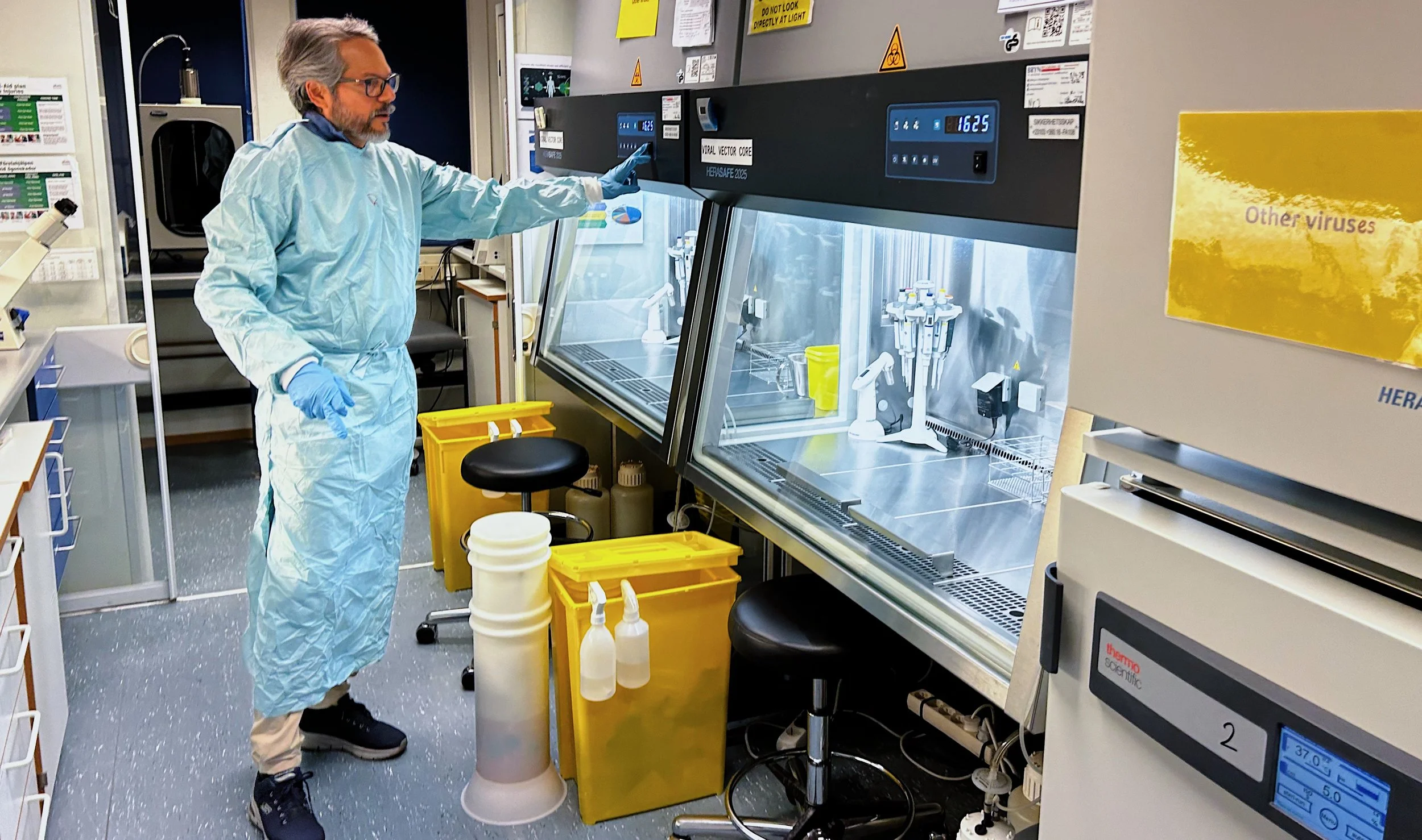 Rajeevkumar Raveendran Nair betjener et ventilasjonsskap på virusvektorlaben. Han har på seg en lyseblå labfrakk og hansker. Fotografi.
