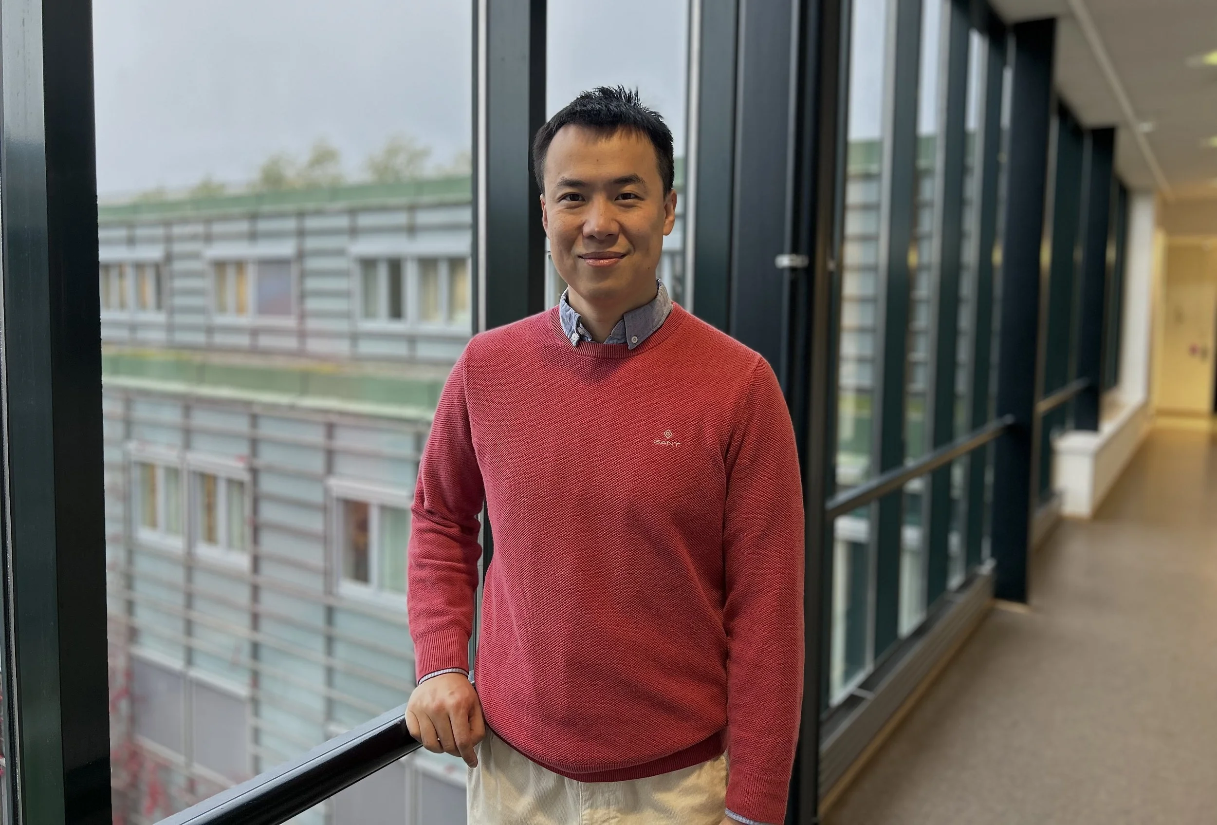 Weijian Zong står lent mot et rekkverk i lokalene til Kavli-institutt for nevrovitenskap. Fotografi.