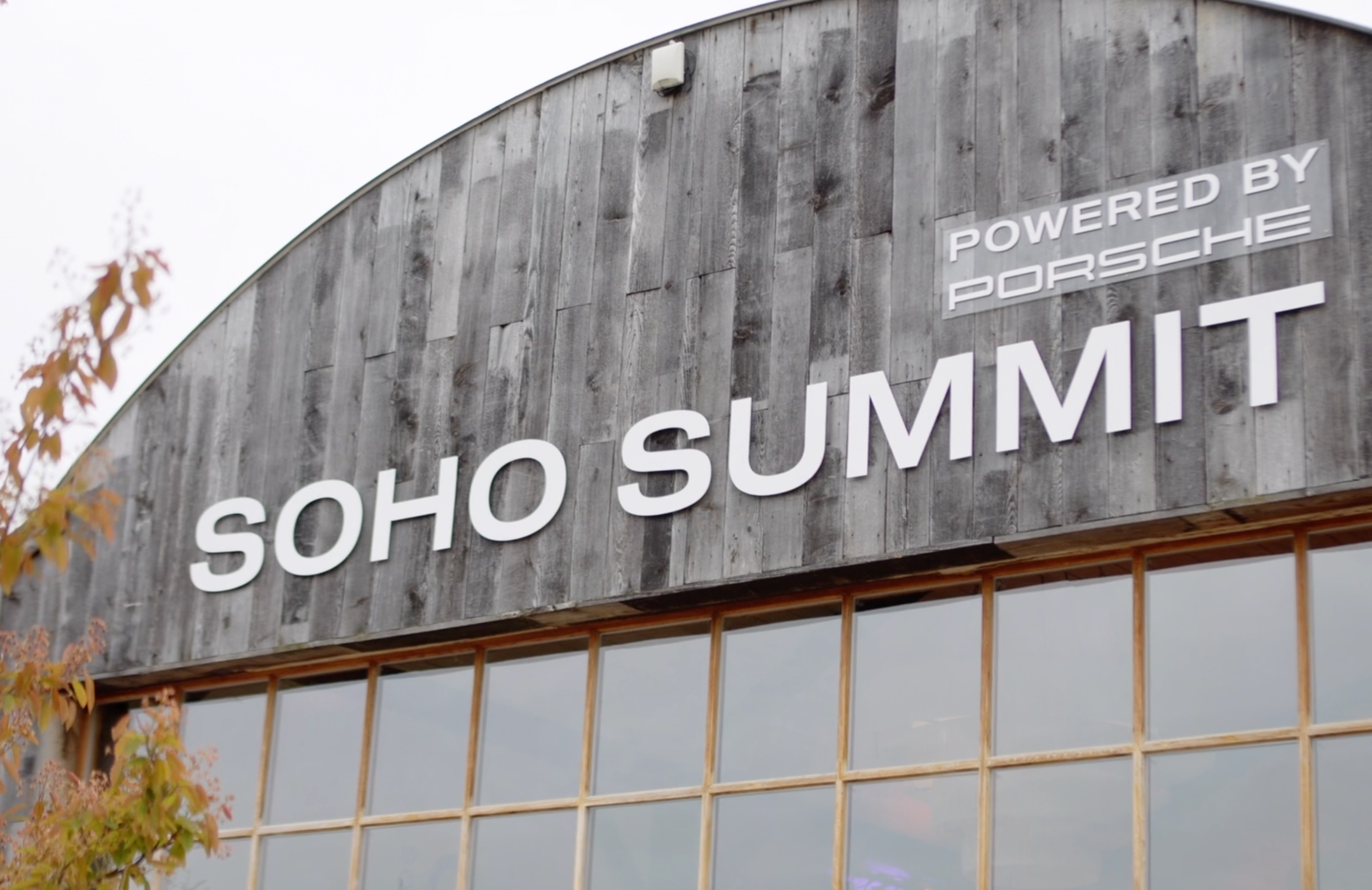 Exterior view of Soho Summit building with wooden facade, large sign reading 'SOHO SUMMIT', and smaller sign 'Powered by Porsche'
