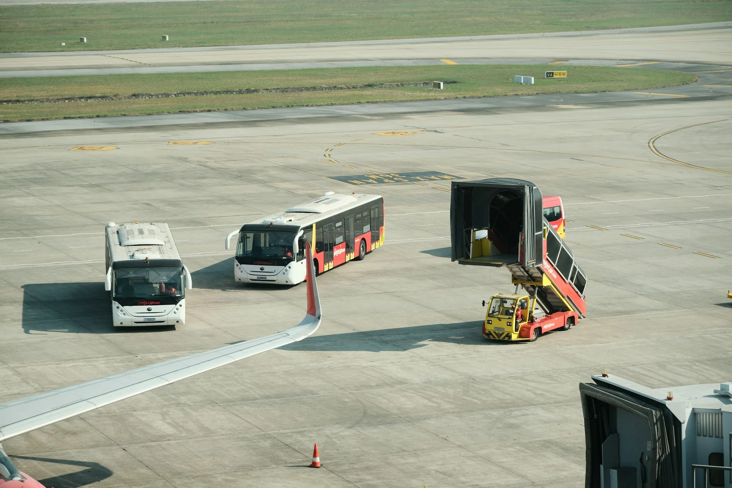 Airport tarmac with buses, jet bridge, and ground service equipment.