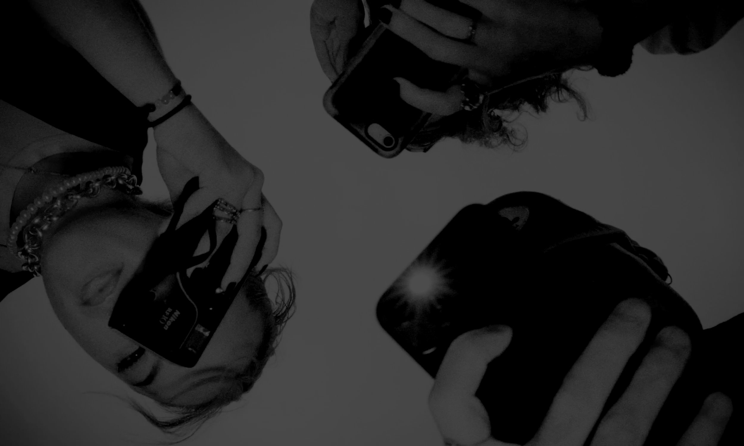 Three people looking down at cameras, with one person holding a camera to their face, and the other two holding smartphones.