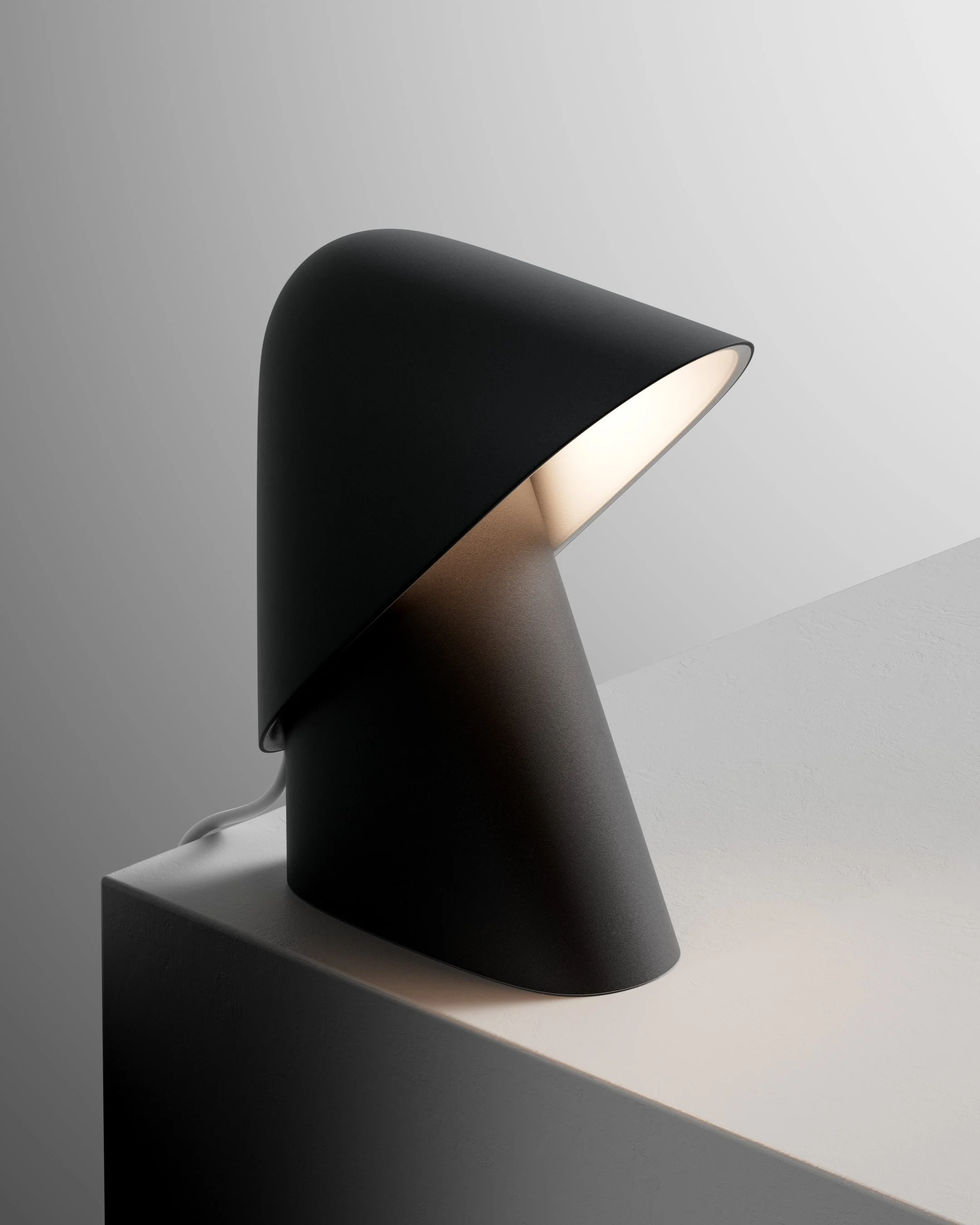 Lampada da tavolo moderna di colore nero con base inclinata, accesa, posizionata su una superficie bianca.