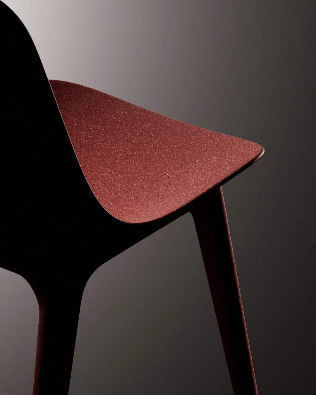 Dettaglio di una sedia moderna con sedile rosso e schienale nero, contro sfondo grigio scuro.