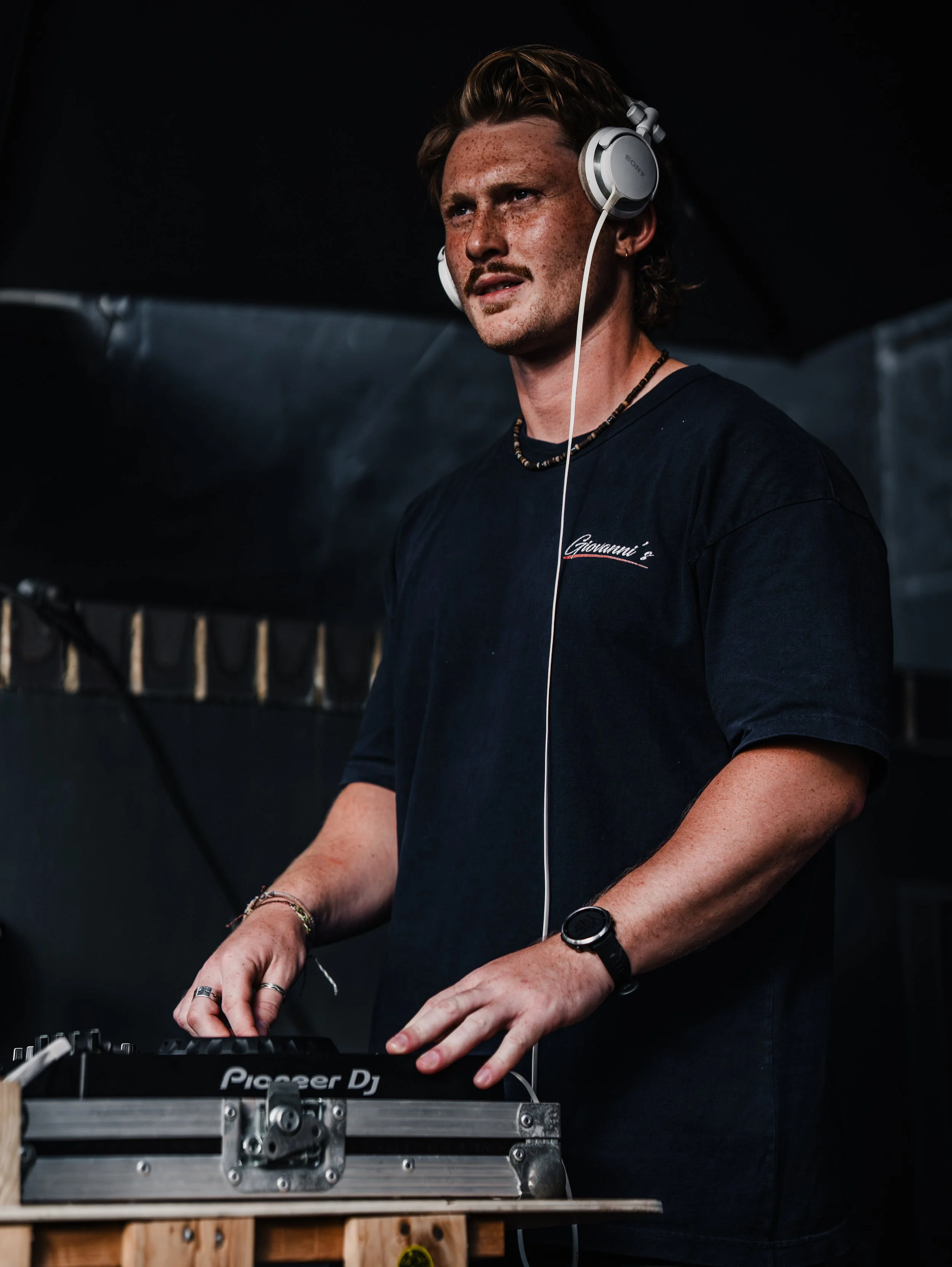 DJ Yann De Galles on his decks wearing headphones and a black top