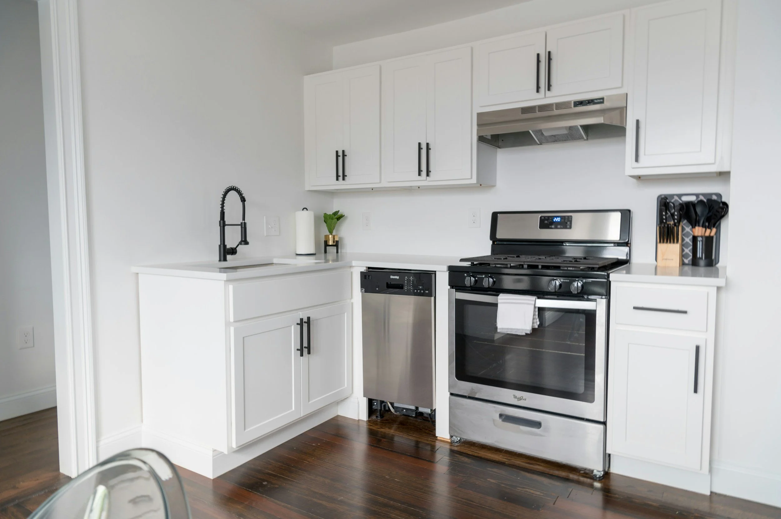 Modern kitchen with white cabinets, black hardware, stainless steel oven, and dark wood flooring.