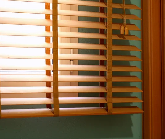 Window with wooden blinds partially open, sunlight coming through.