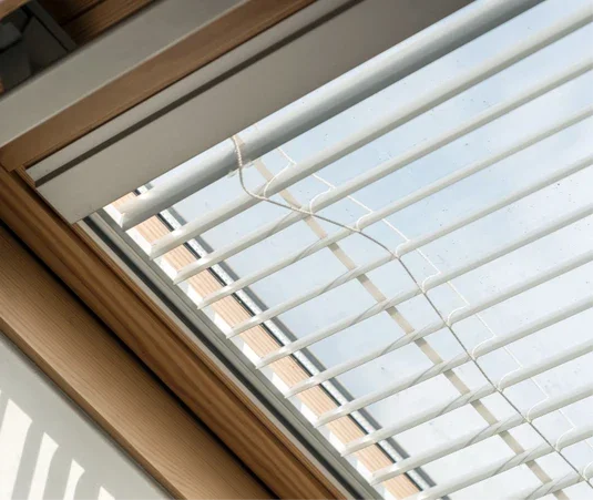 View of a window with white blinds and a wooden frame, showing an overcast sky outside.