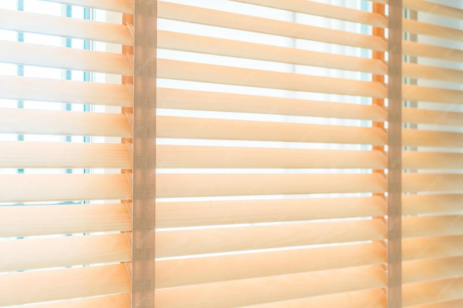 Close-up of beige wooden blinds with sunlight filtering through.