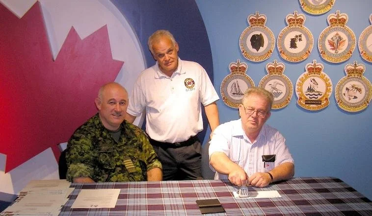 Colonel GMA Morey, left and Museum Curator, Bryan Nelson, center look on as Canada Post representative, Laurie Doyle