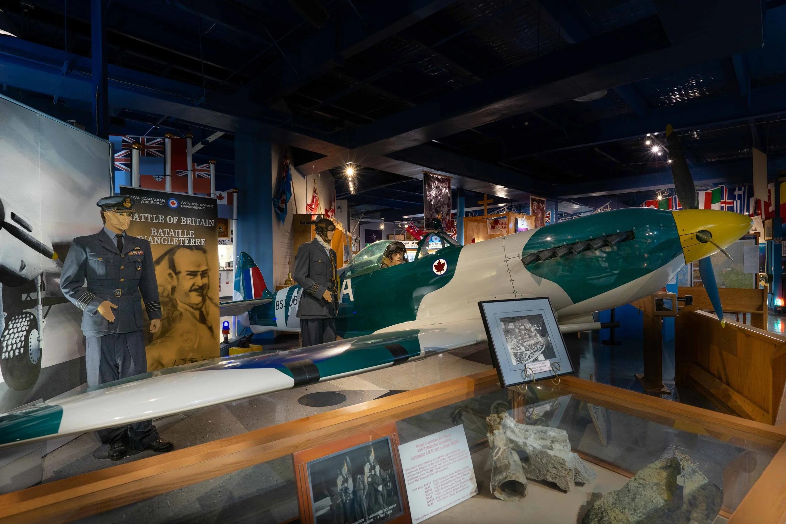 A museum exhibit featuring a vintage Canadian military aircraft, mannequins in historical military uniforms, and various display artifacts with informational plaques and flags in the background.