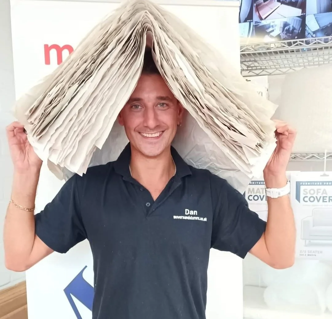 A man with a smile wearing a black shirt holds a large stack of papers above his head, creating a tent-like structure.