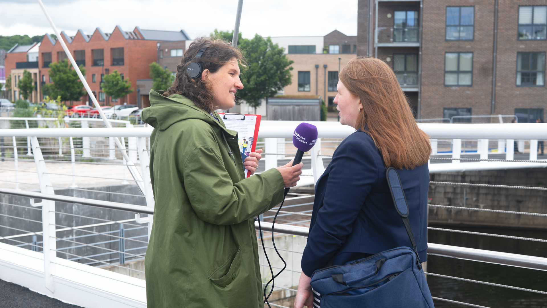 A female reporter holding a microphone labeled BBC Radio Nottingham interviewing a Radiant Cleaners employee near Nottingham's new waterway bridge project.