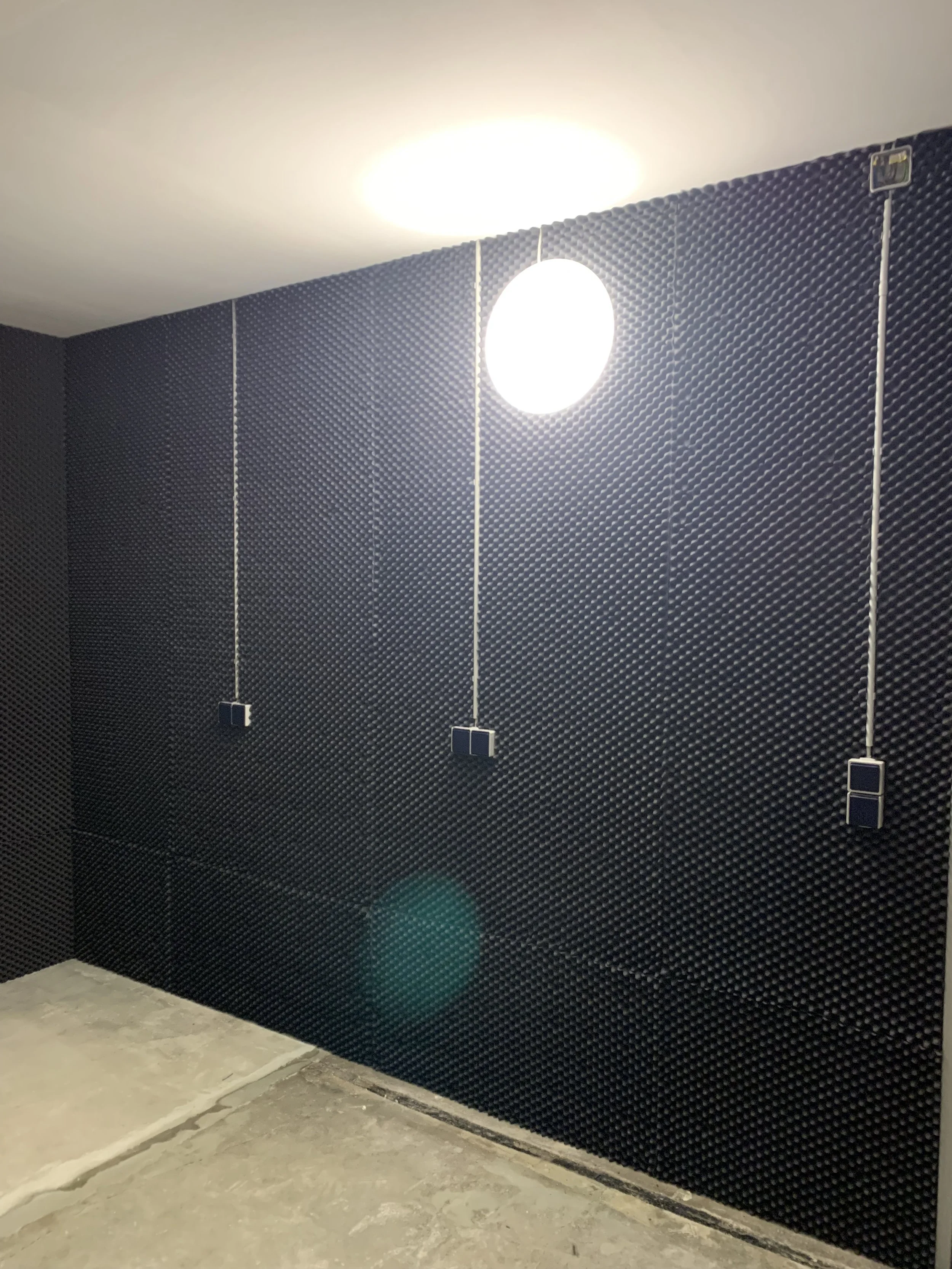 Ein Raum mit schwarzen schallabsorberplatten an der Wand, drei Deckenleuchten und Kabel mit Steckdosen.