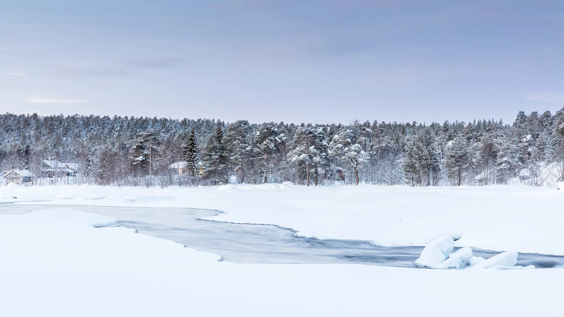 Paysage enneigé avec forêt de conifères à Reykjavik en Islande, lac gelé et quelques maisons en arrière-plan sous un ciel clair.