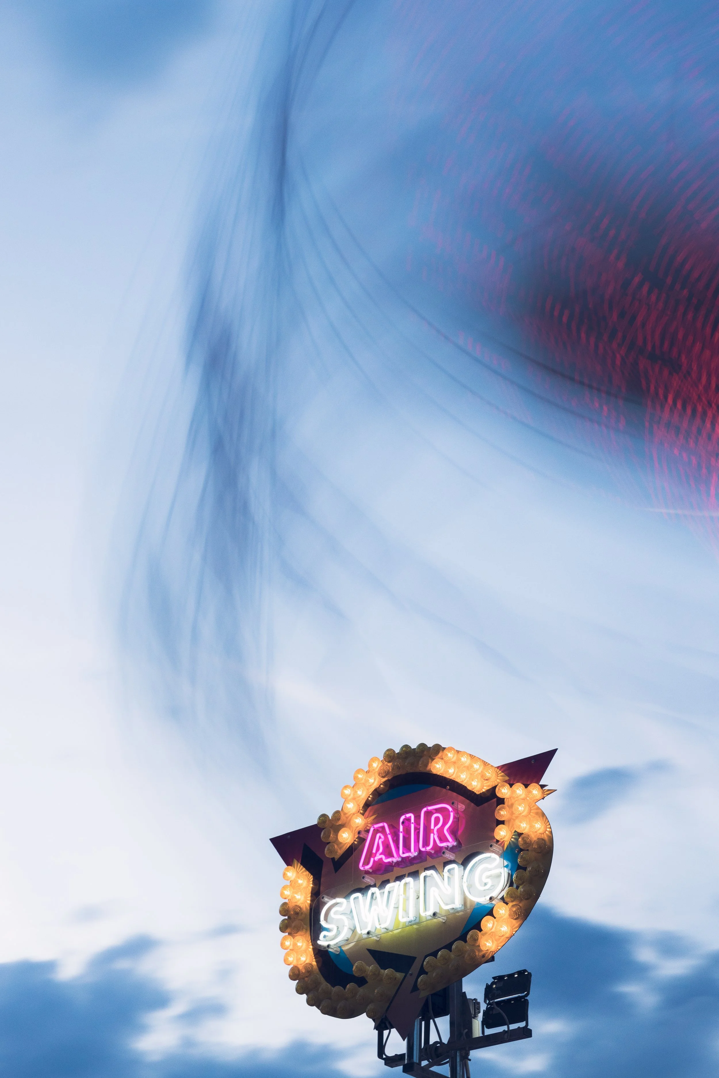 Fête foraine au jardin des tuileries à Paris. Panneau lumineux avec les mots 'Air Swing' entouré de lumières et d'un joli mouvement de flou de bougé, suspendu en extérieur avec un ciel en arrière-plan.