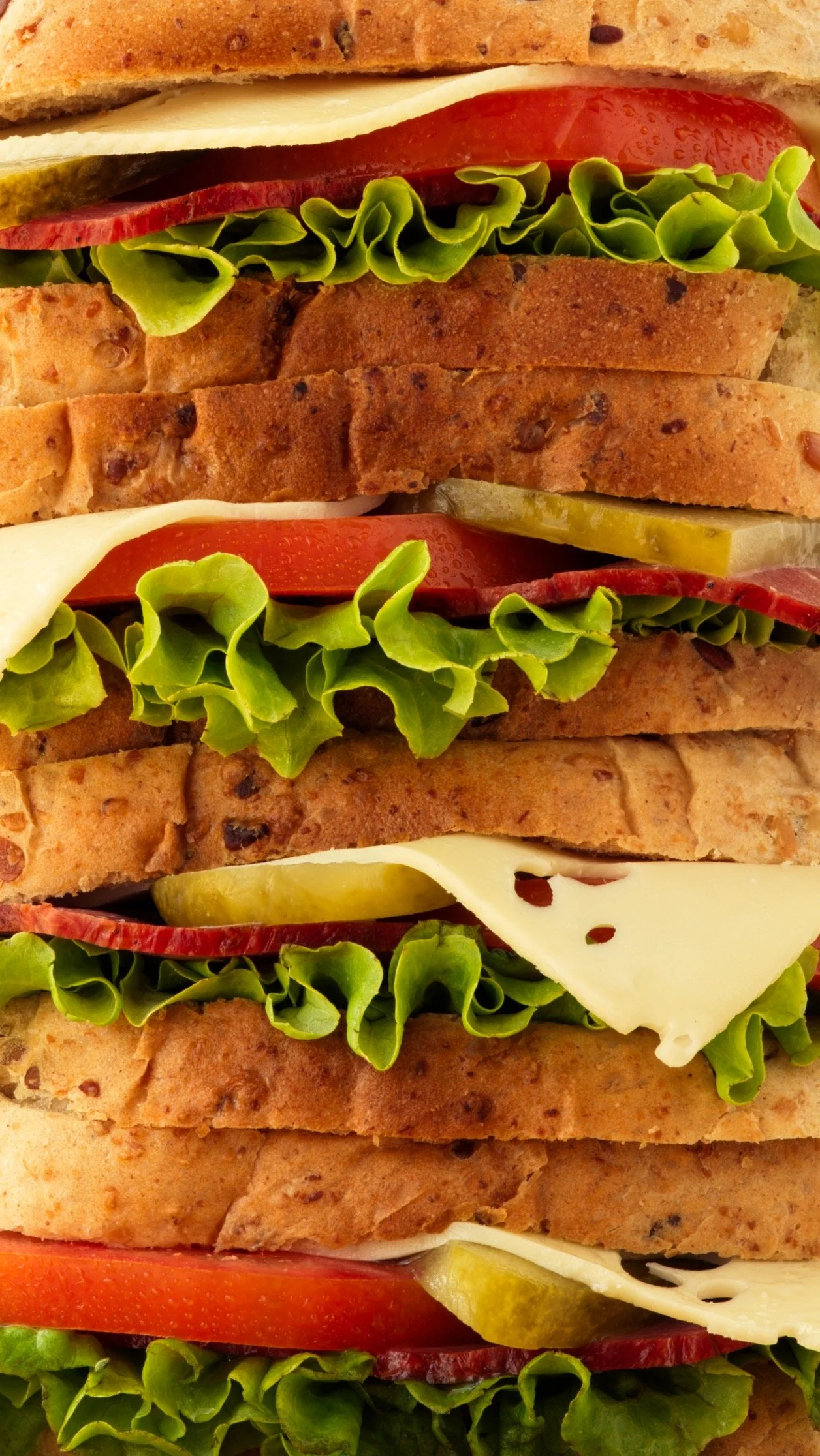 Sandwichs multistrates avec laitue, tomate, fromage, boeuf, cornichons et pain.
