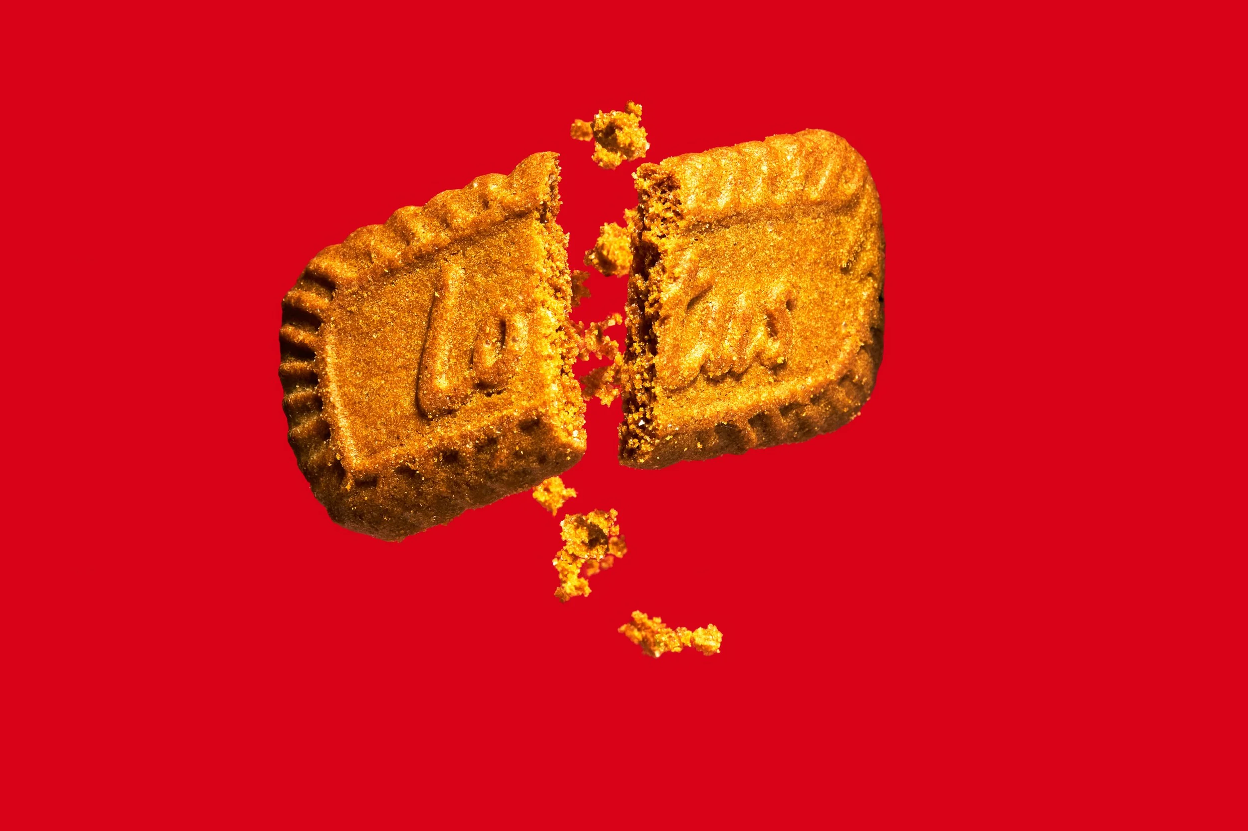 Un biscuit lotus brisé avec des miettes éclatant sur un fond rouge.



