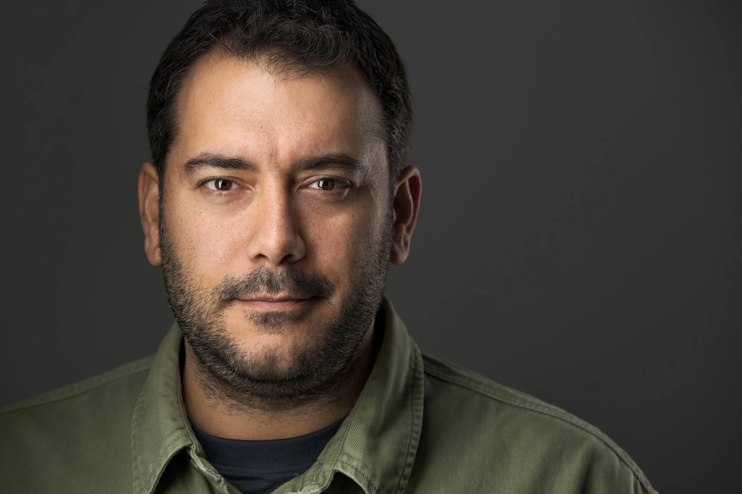 Portrait haut de gamme d'un homme avec barbe, portant une chemise vert foncé carhartt , fond gris foncé.