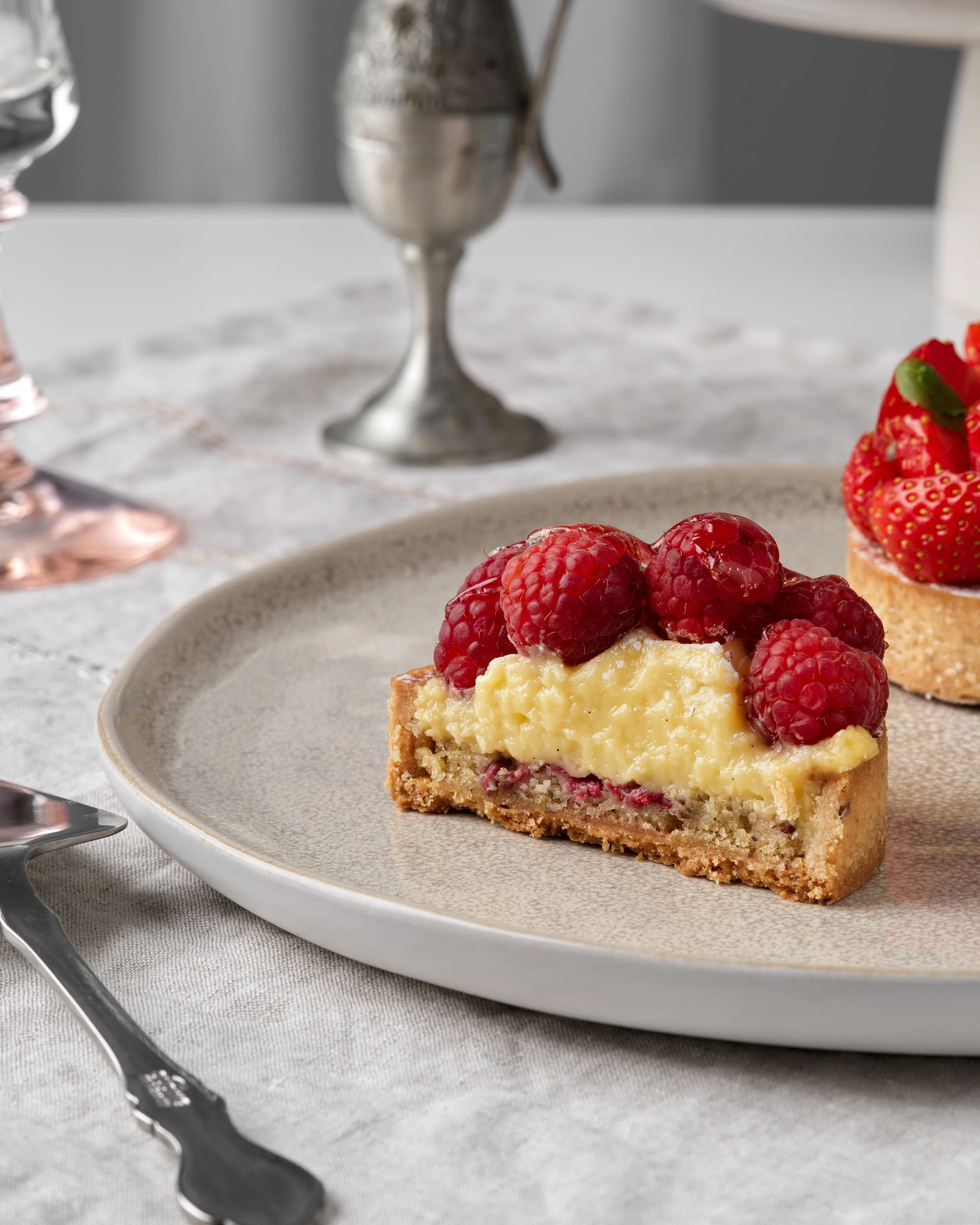 Une part de tartelette aux framboises sur une assiette beige, au centre d'une table avec un décor sobre et élégant.