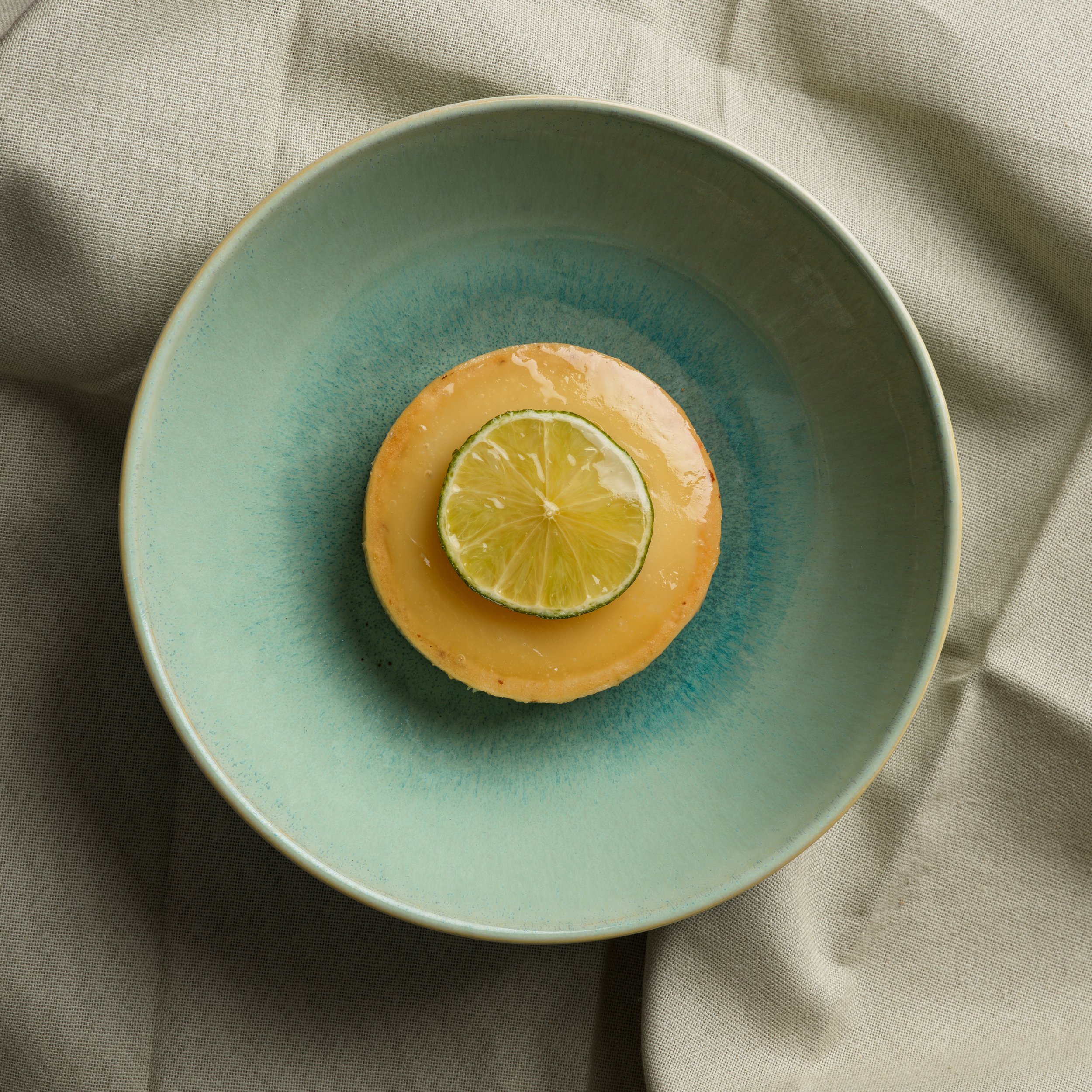 Tartelette au citron dans une assiette en céramique verte, posée sur une nappe beige..