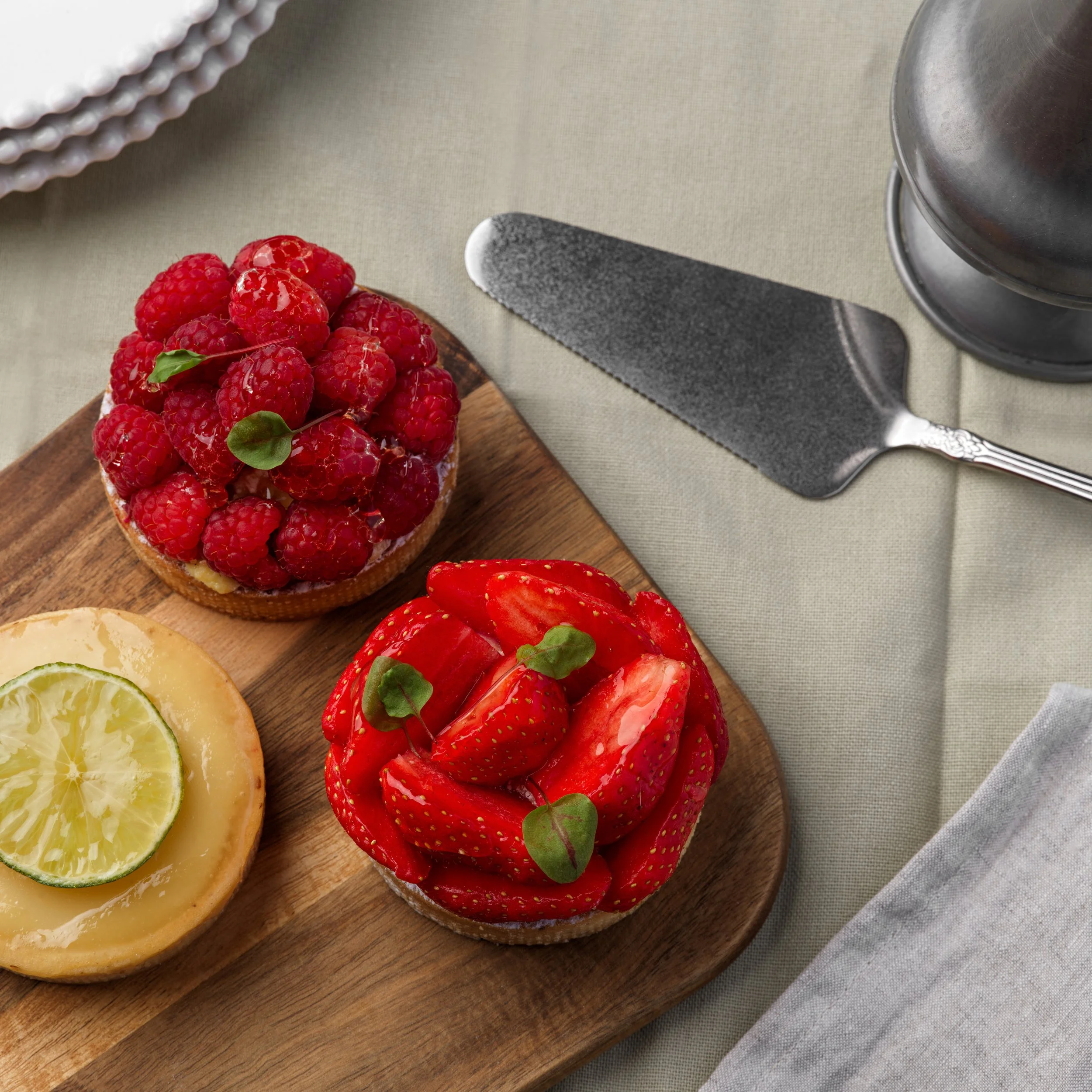 Plateau de tartelles aux fruits avec un glaçage brillant, posé sur une planche en bois, sur une table avec un décor sobre et élégant.