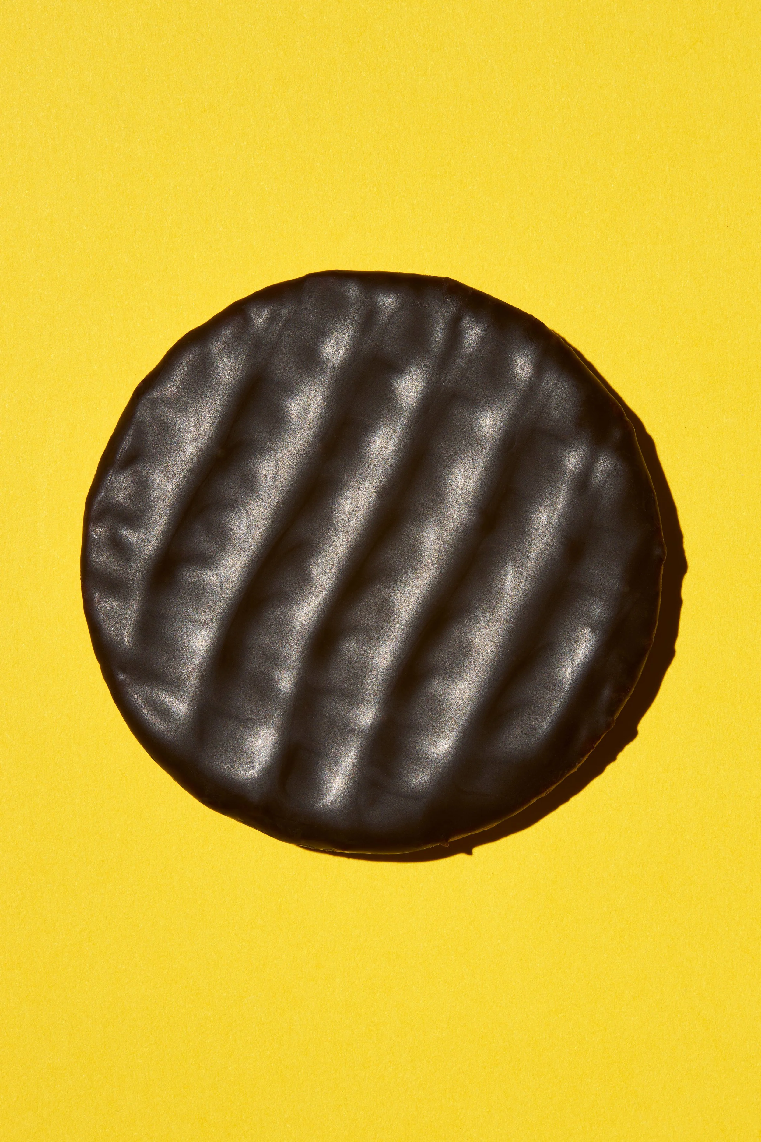 Un biscuit rond noir avec une texture ondulée, placé sur un fond jaune vif.