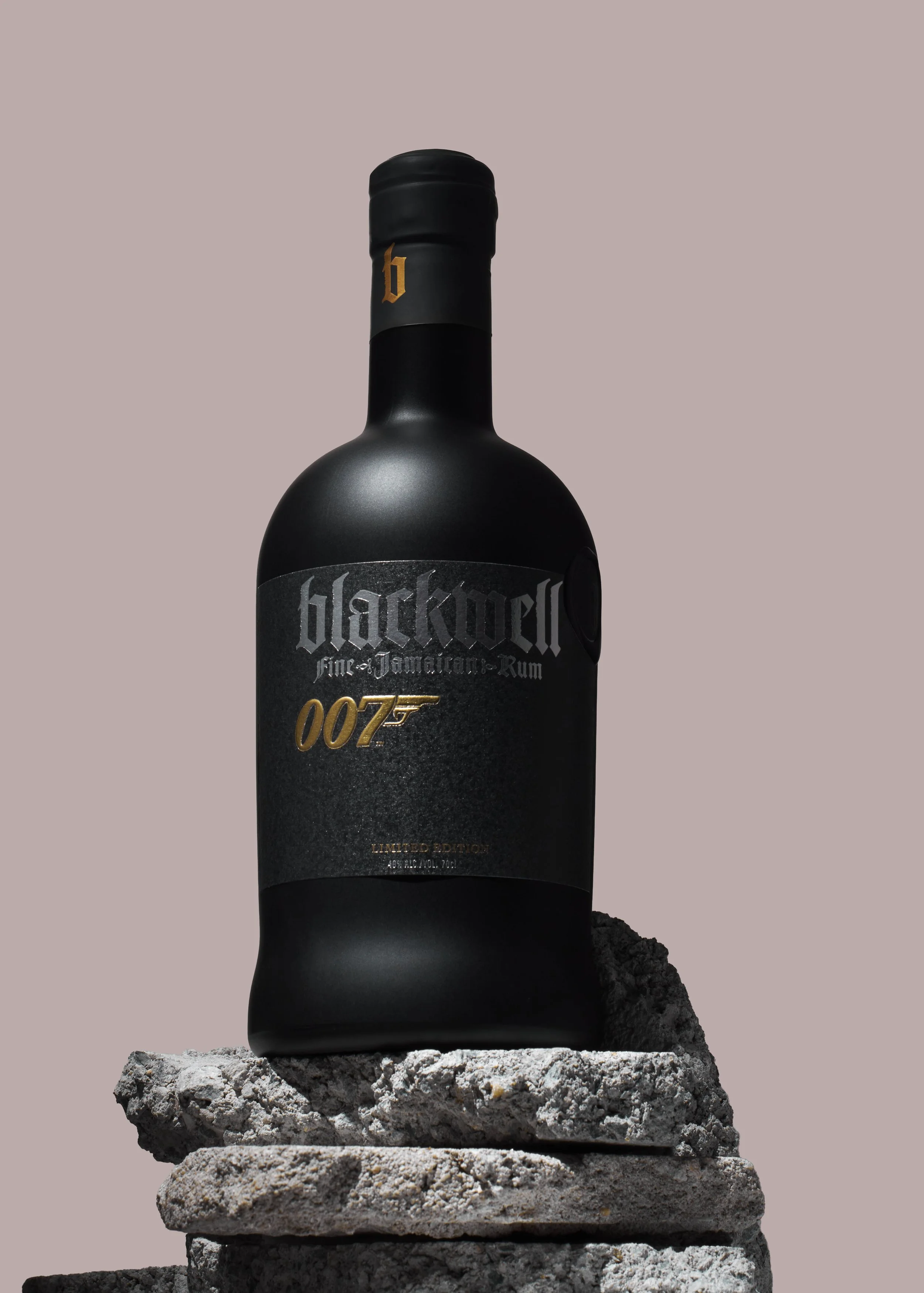 Une bouteille noire de rhum Blackout, édition limitée, posée sur des pierres grises, avec un fond beige mauve pale.