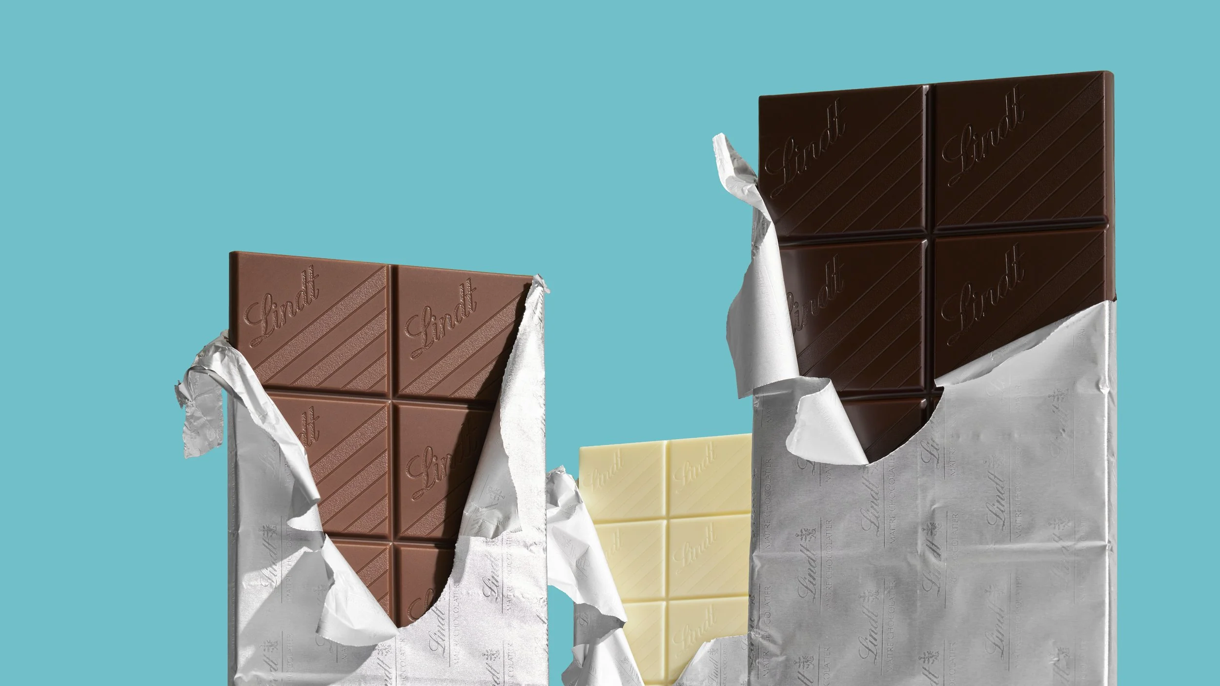 Trois tablettes de chocolat, une blanche et deux au lait, partiellement déballées sur un fond bleu.