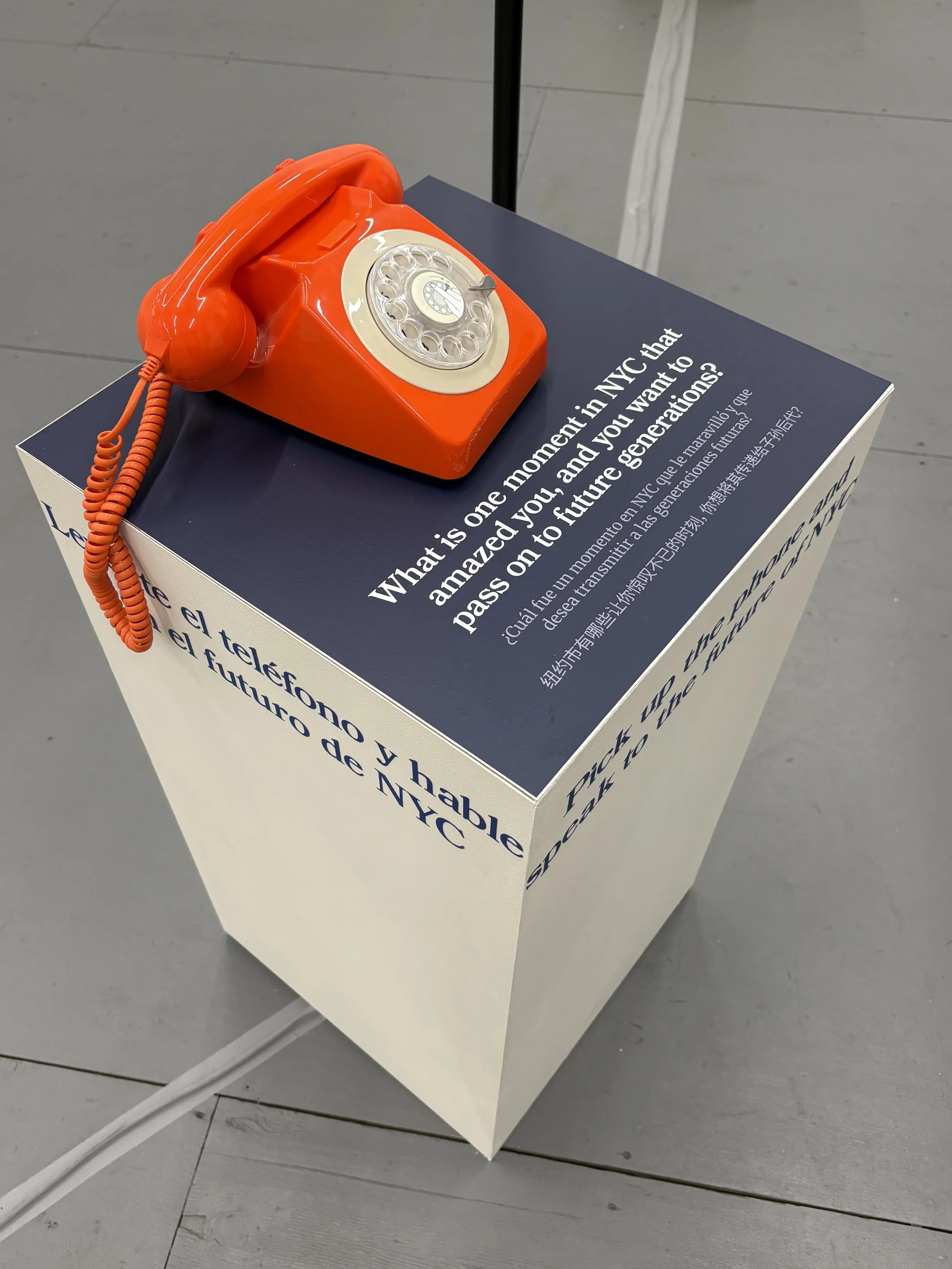 An orange rotary dial telephone placed on top of a dark blue and white display stand with text discussing the future of telecommunications.
