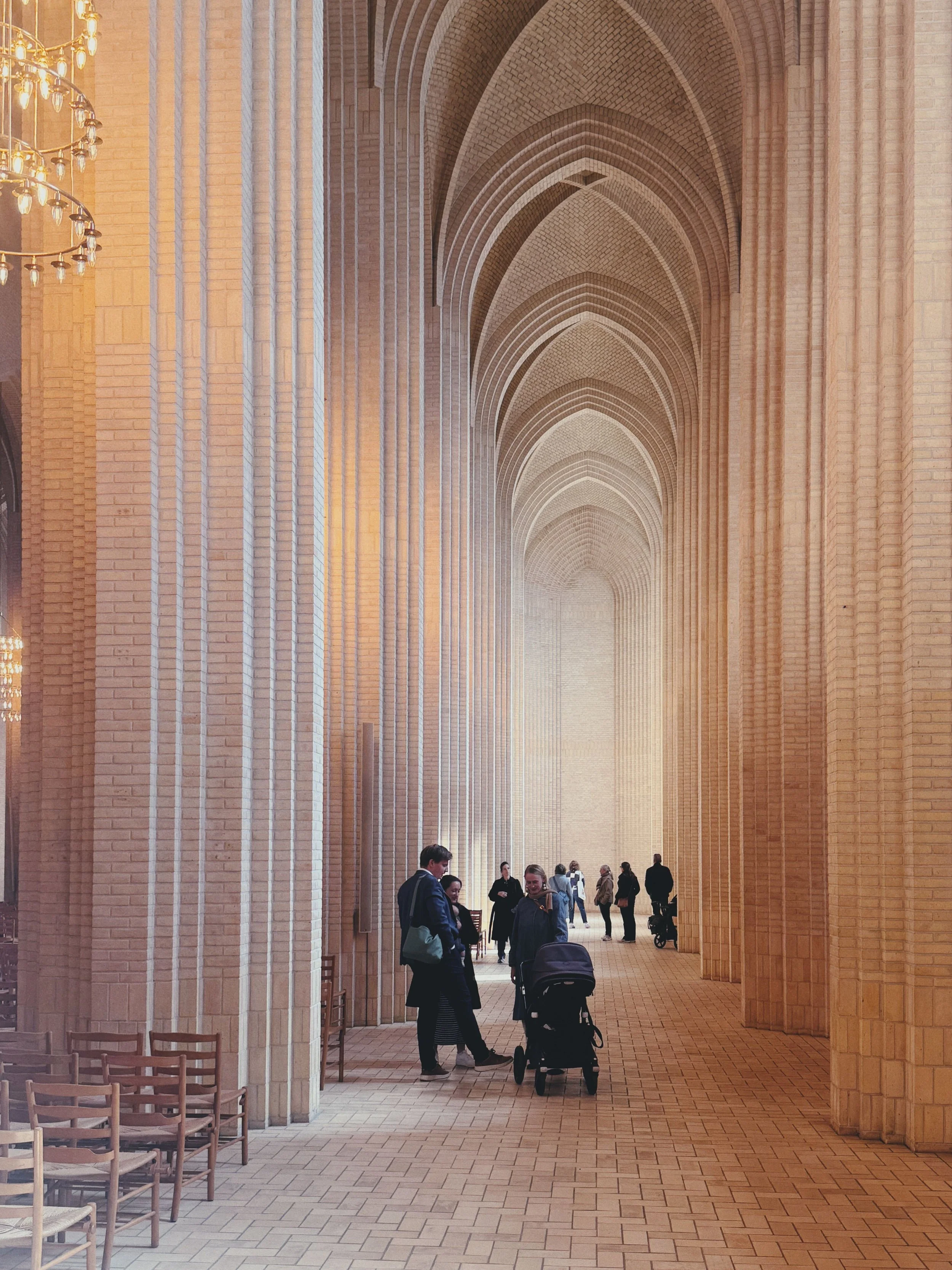 People walking and chatting in a large hall with high vaulted brick ceilings and tall brick columns.