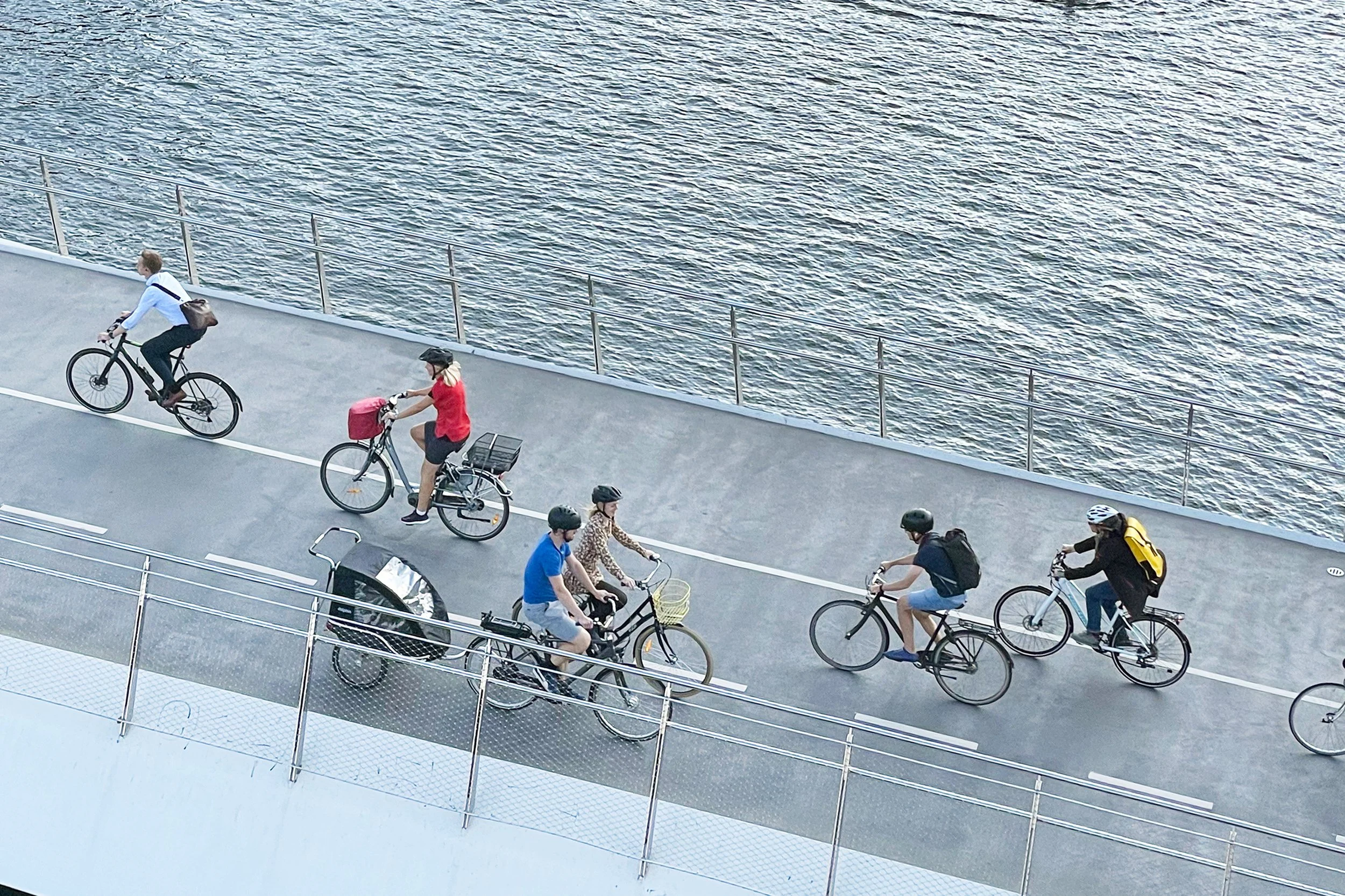 People riding bicycles on a coastal bike path beside the water.